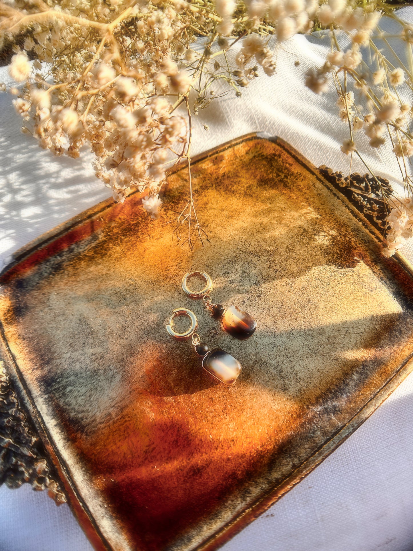 Pair of Agate and Obsidian Golden Hoop Earrings on a textured brown surface with dried flowers in the background