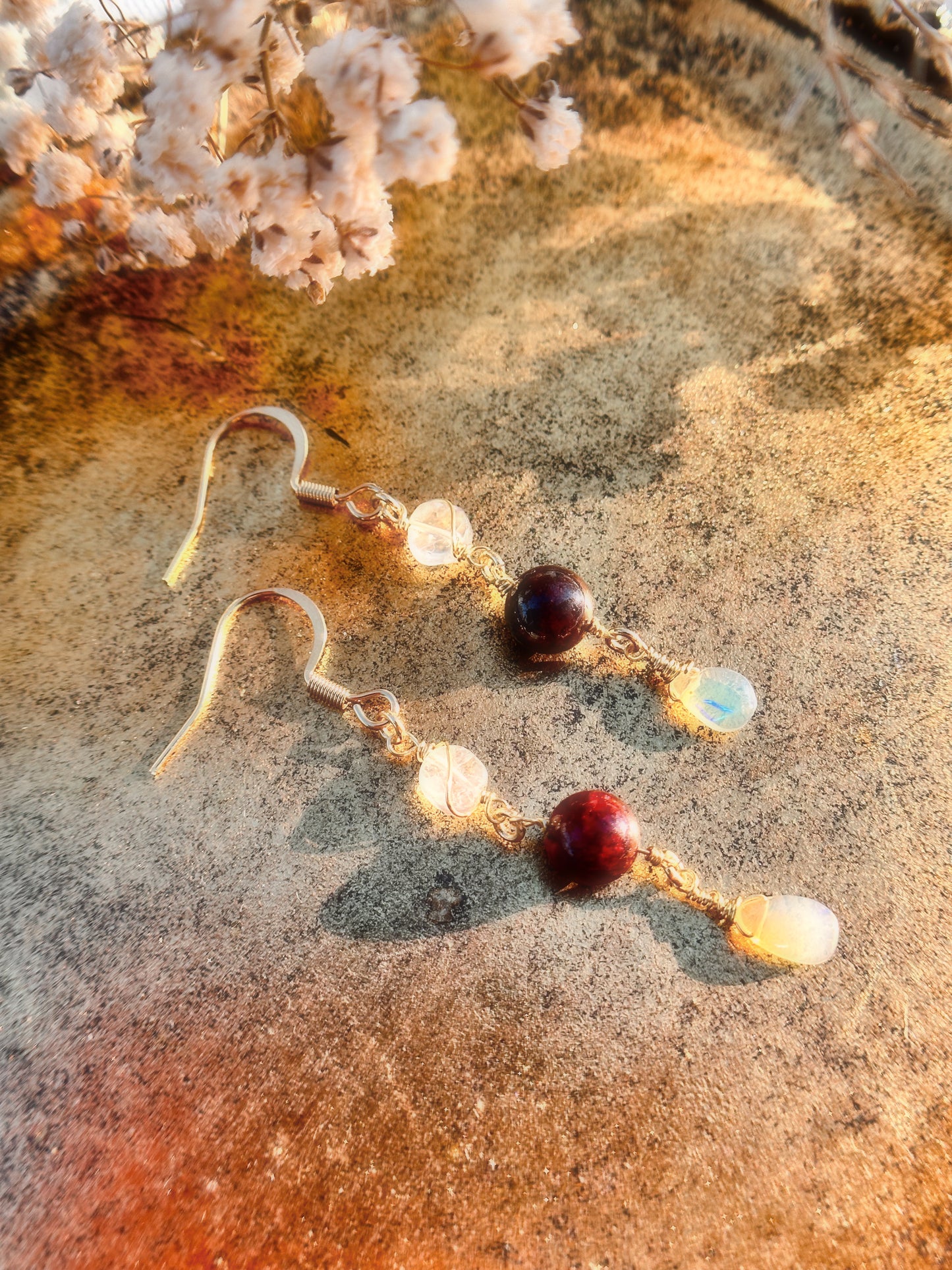 Gold Stainless Steel with Rainbow Moonstone, Ethiopian Opal and Garnet crystals on a gold stand against a neutral brown background with dried flowers.