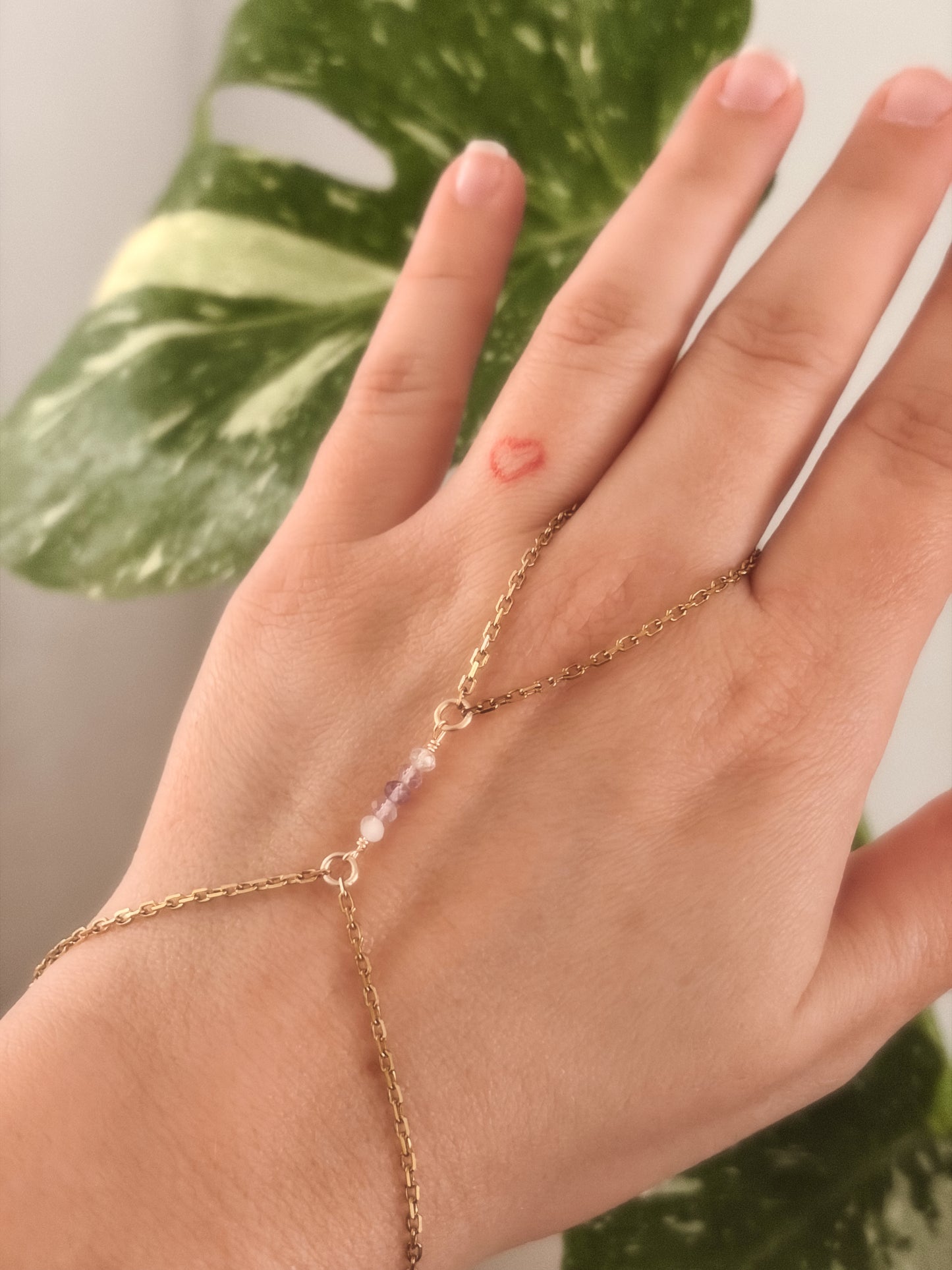 Gold Stainless Steel tarnish resistant handchain with Fluorite crystal beads on a person's hand against a blurred background with a monsterra plant.