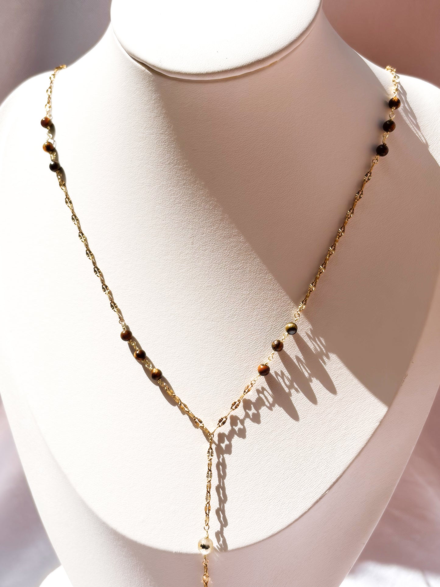 Close up of Gold Stainless Steel Lip Chain necklace with Tiger Eye beads on a white stand against a light background
