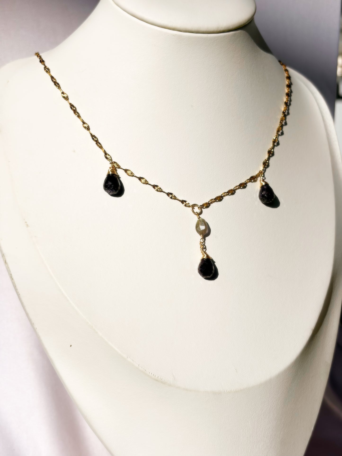 A gold chain necklace with three teardrop-shaped Sapphire stone pendants and a central Labradorite bead detail, displayed on a white jewelry bust.