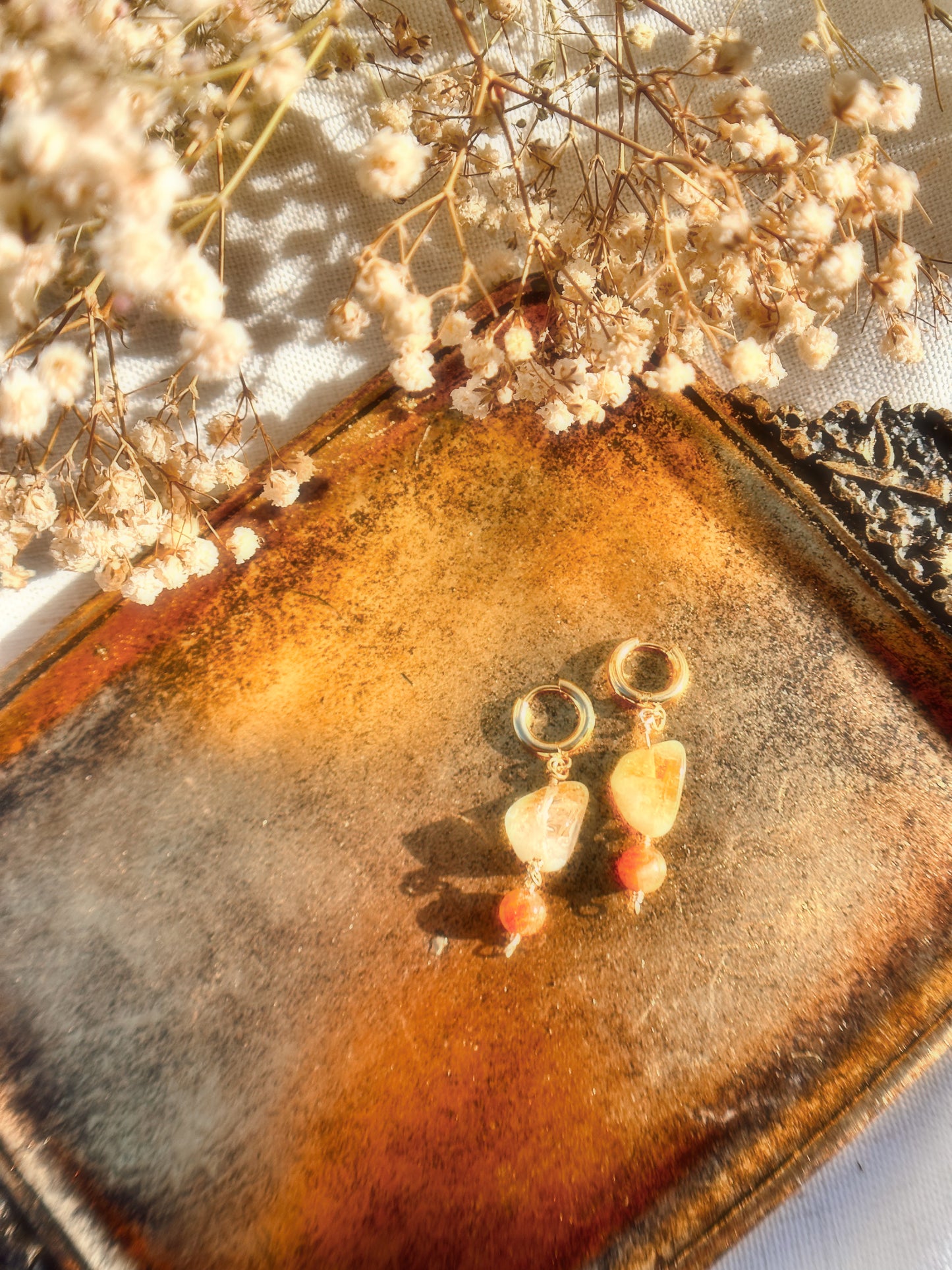 Pair of Stainless Steel Gold earrings with Citrine and Sunstone crystals on a gold stand against a dried flower background
