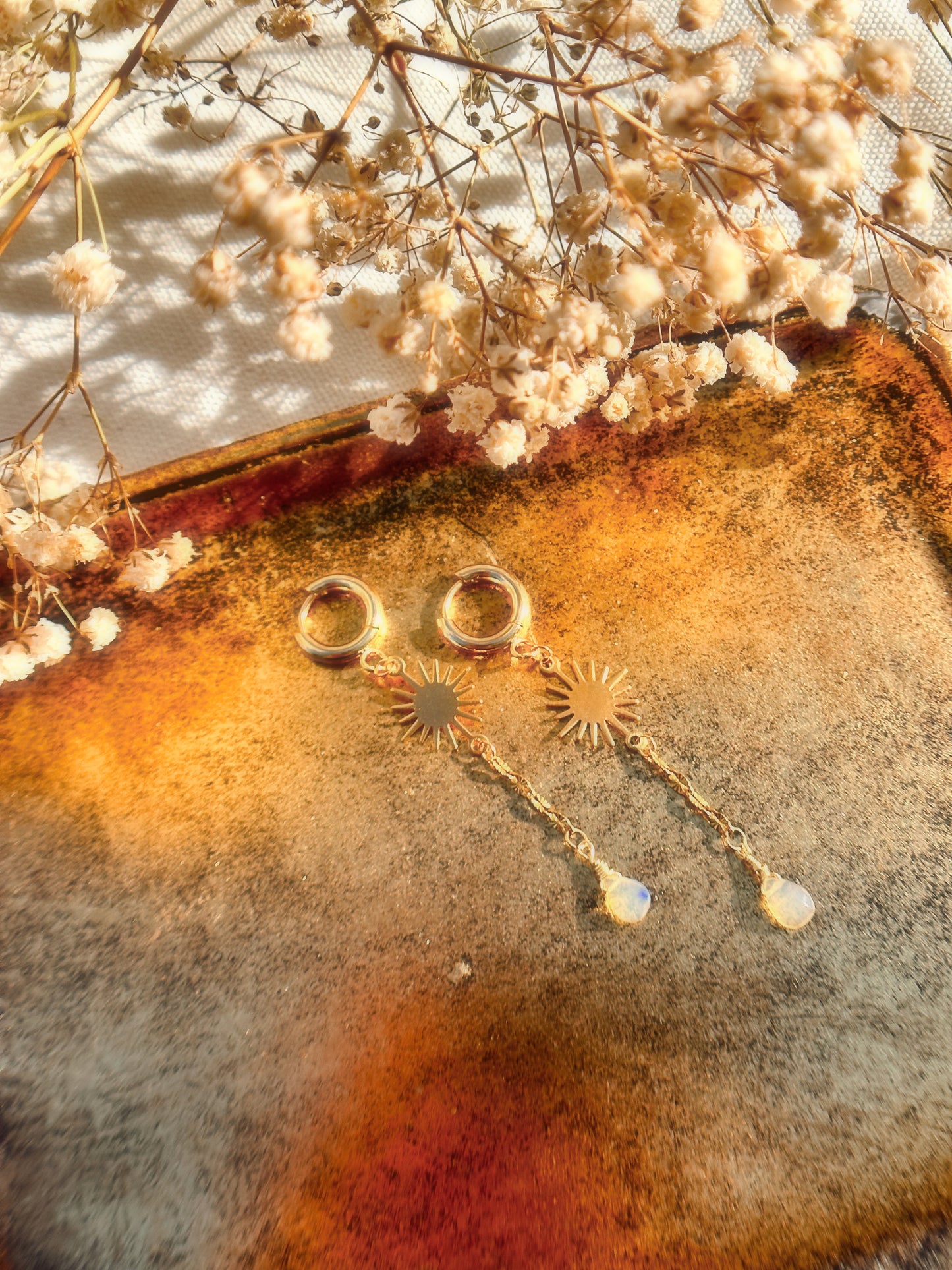 Gold Stainless Steel Ethiopian Opal earrings with Sun charms on a floral background.