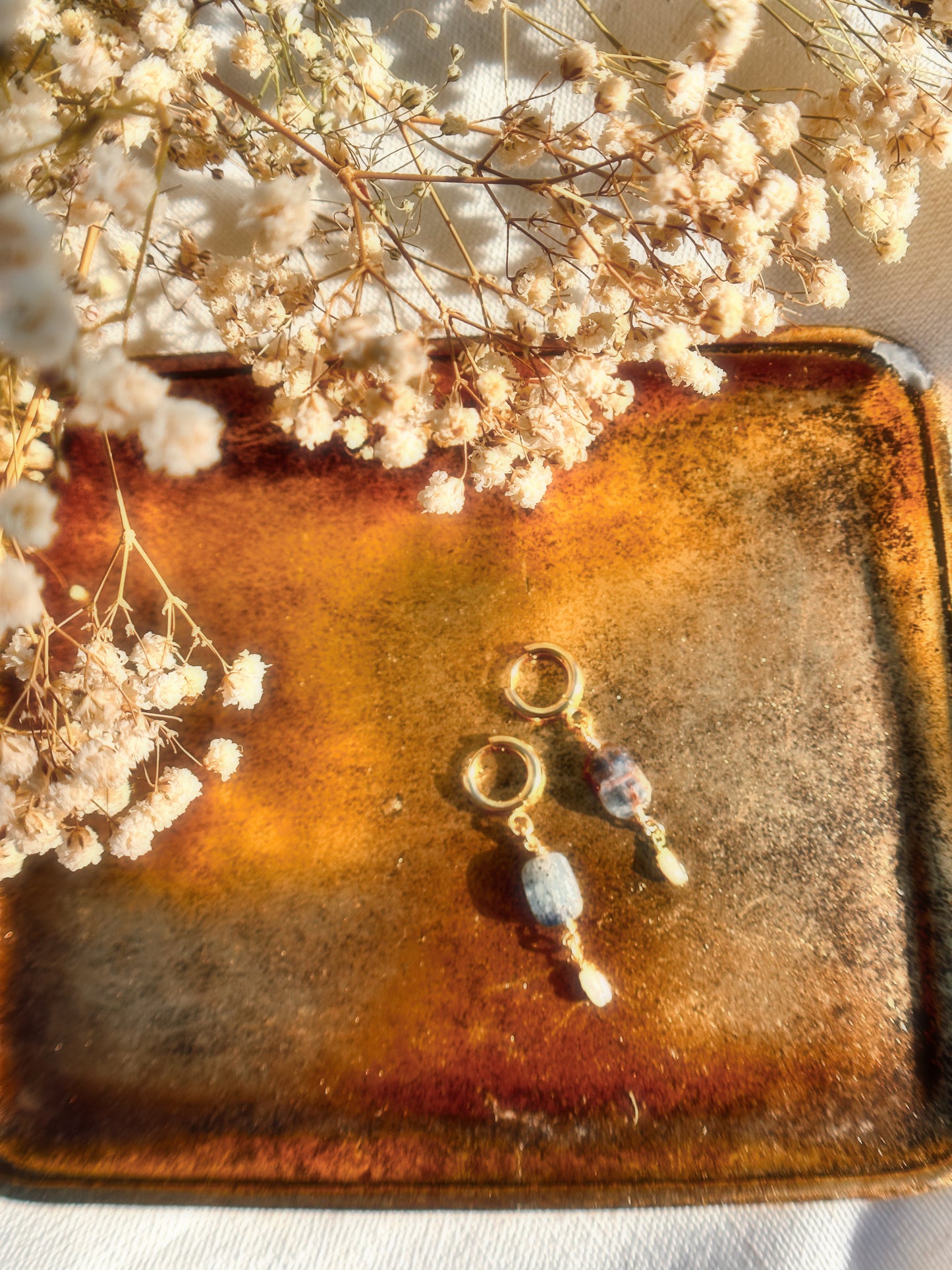 Gold Stainless Steel earrings with Blue Kyanite and Faux Pearl gemstones with a brown and floral background.