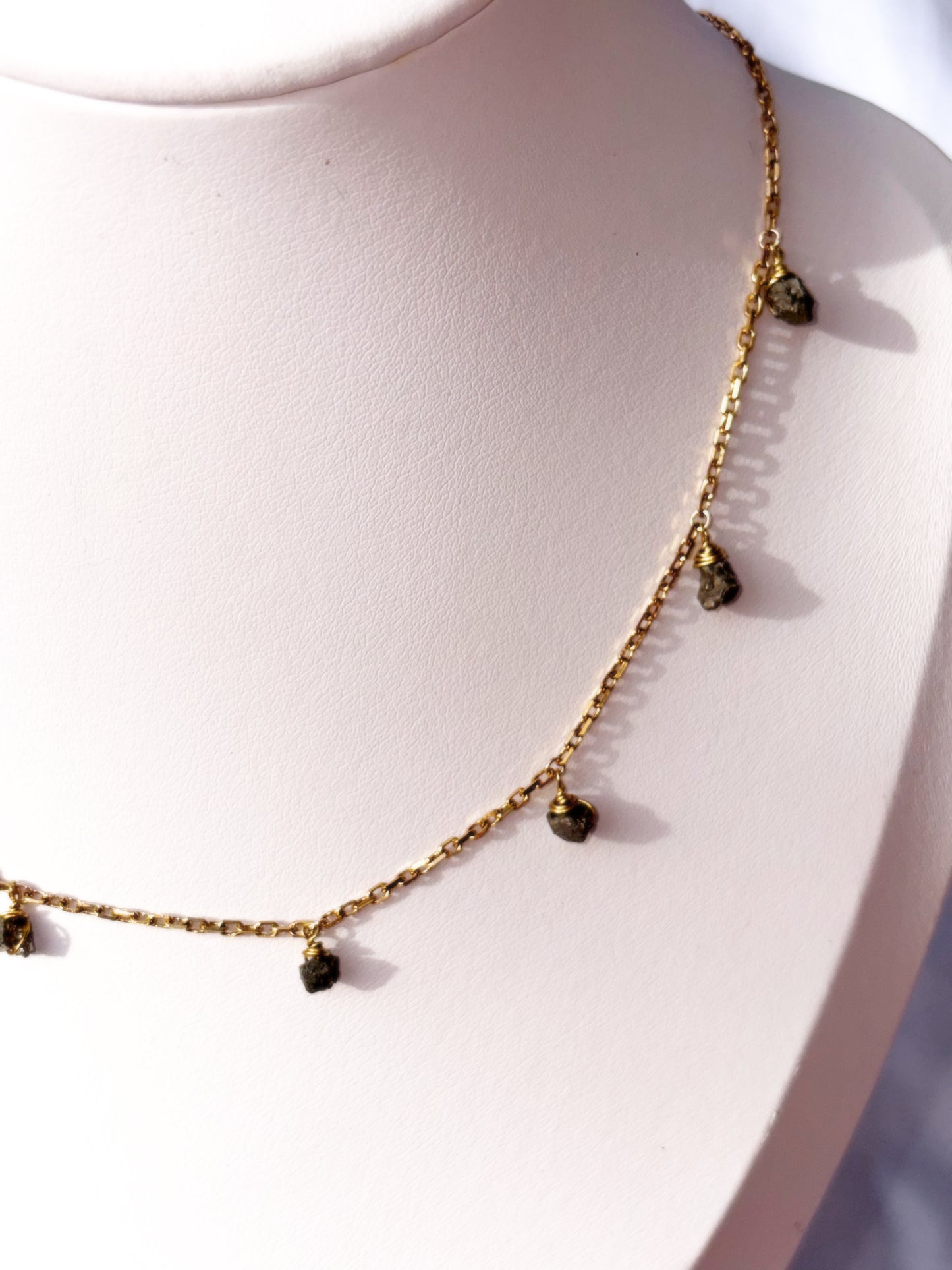 Close up of Stainless Steel Gold necklace with small Pyrite raw crystal gemstone beads stones on a white stand.