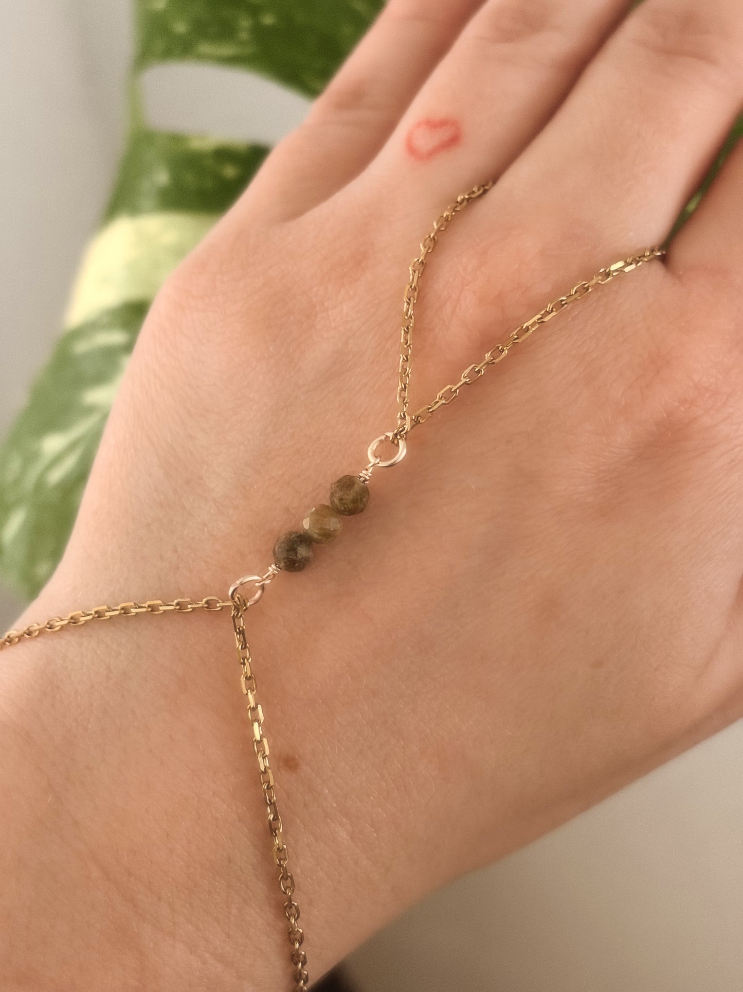 Gold Stainless Steel tarnish resistant handchain with Green Garnet crystal beads on a person's hand.