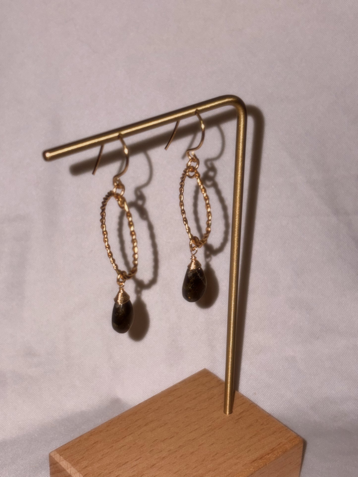 Gold earrings with Labradorite gemstones on a gold stand against a light background.
