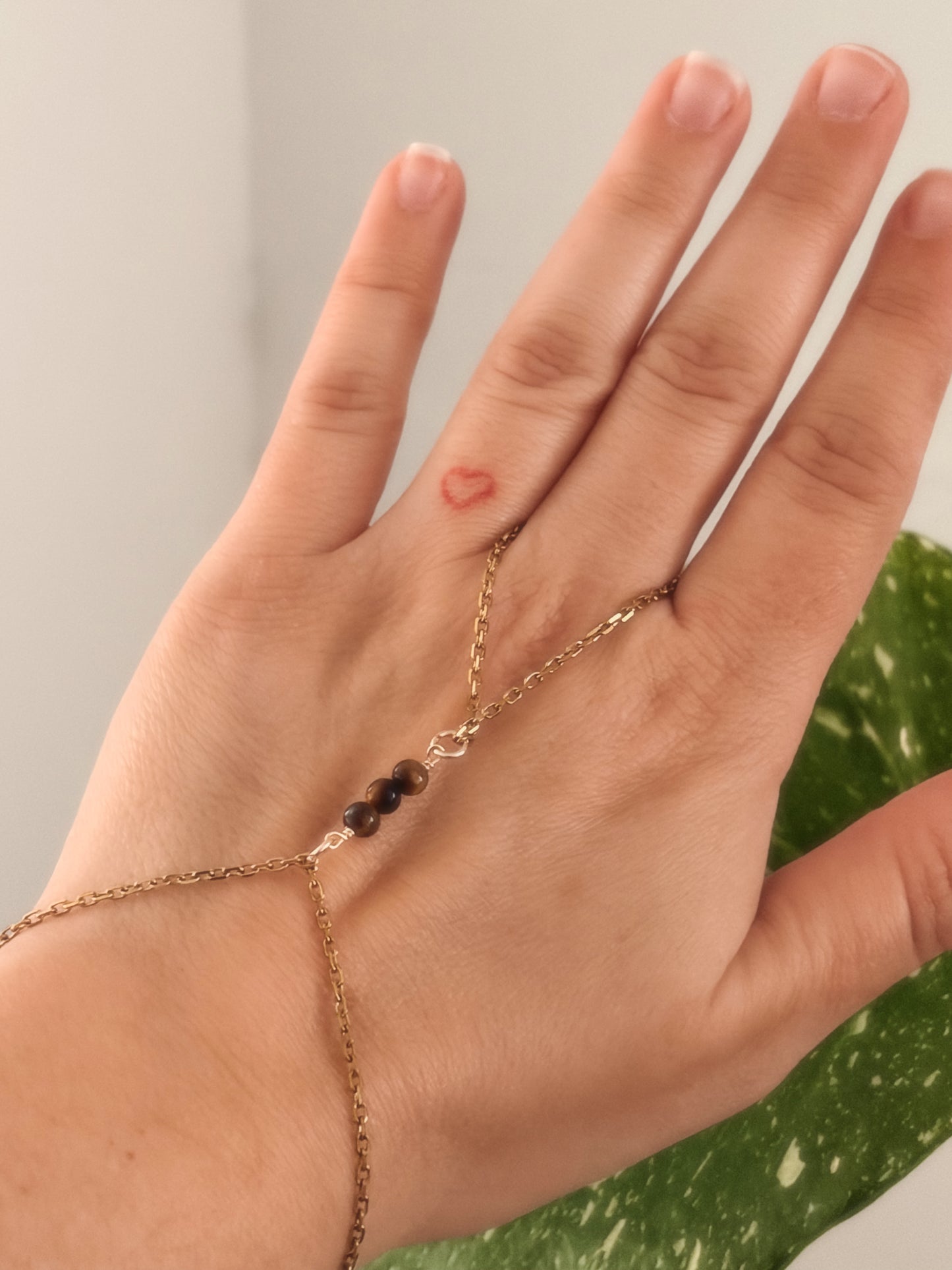 Gold stainless steel handchain bracelet with Tiger Eye beads on a person's wrist against a neutral background.