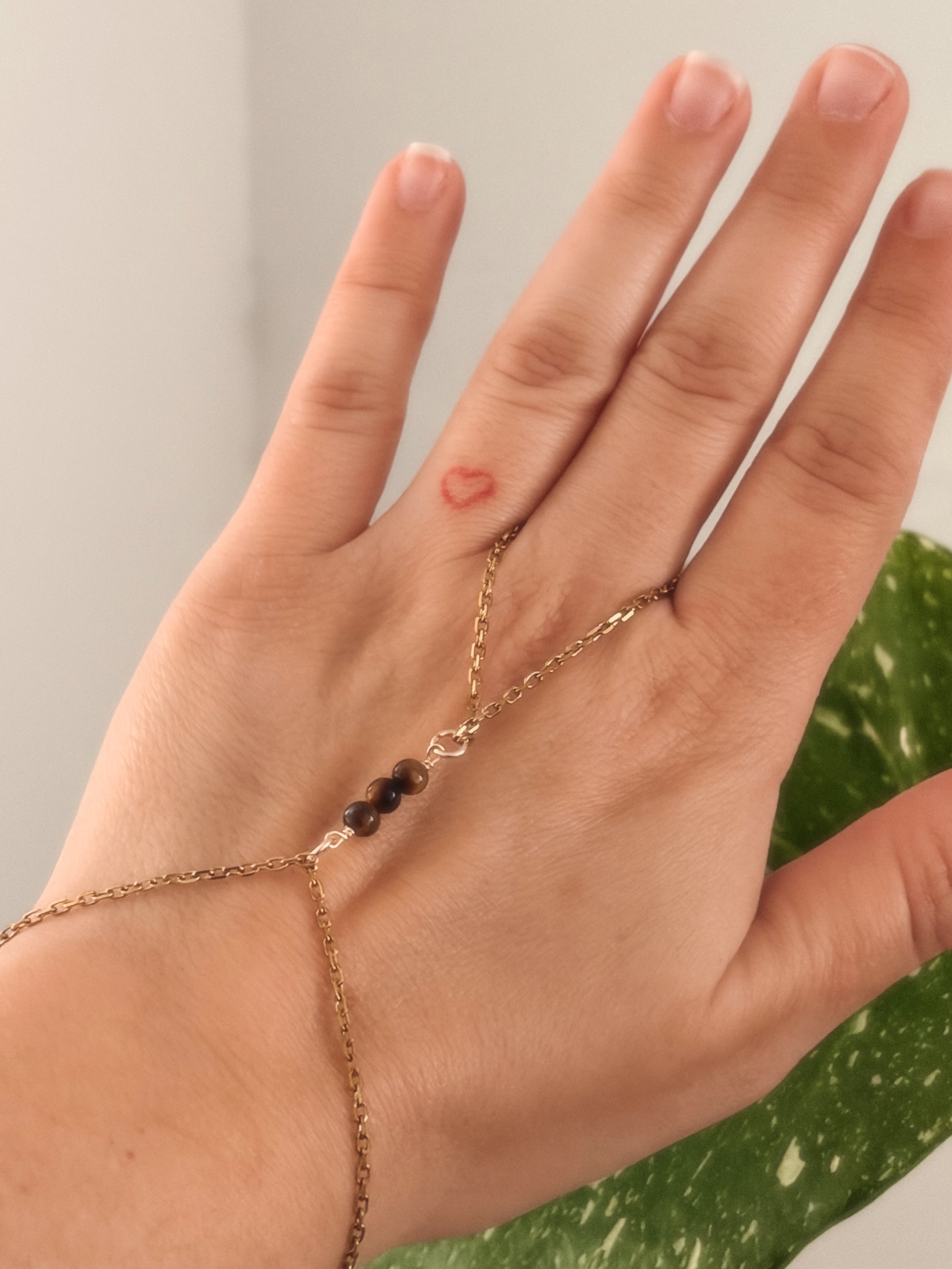 Gold stainless steel handchain bracelet with Tiger Eye beads on a person's wrist against a neutral background.