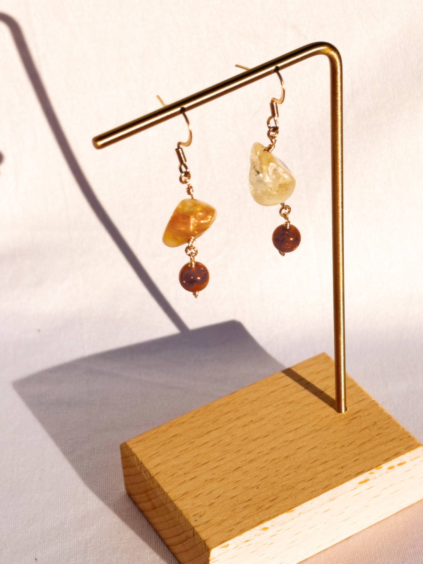 Pair of Stainless Steel Gold earrings with Citrine and Sunstone crystals on a gold stand against a light background