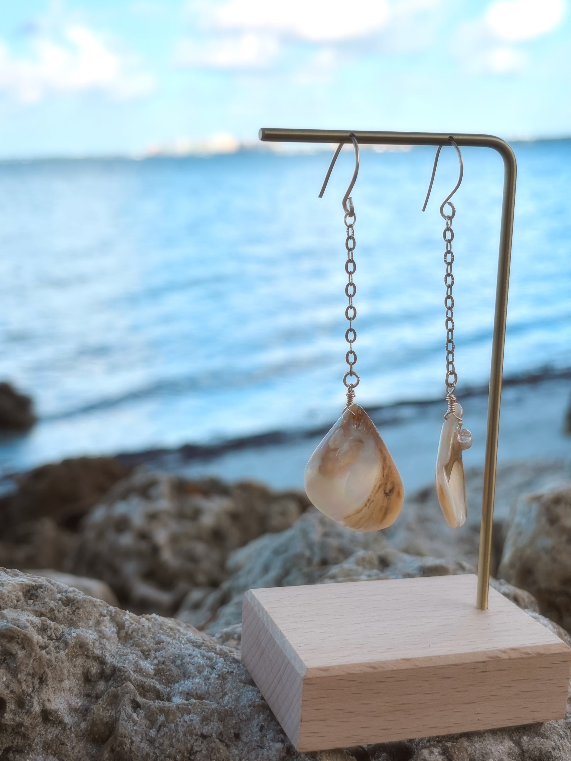 Beach close up of stainless steel dangly gold pearl/shell earrings.