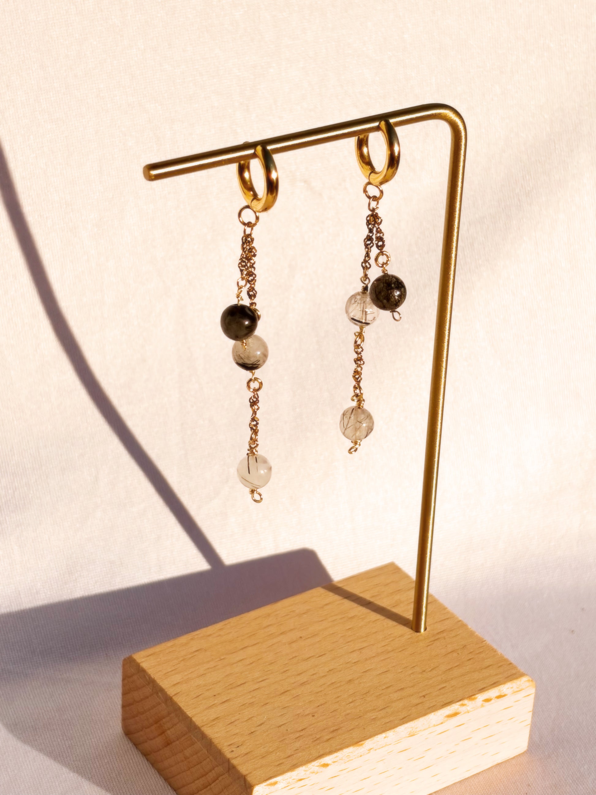 Black Rutilated Quartz Dangly Earrings on a Gold Stand with a white background.