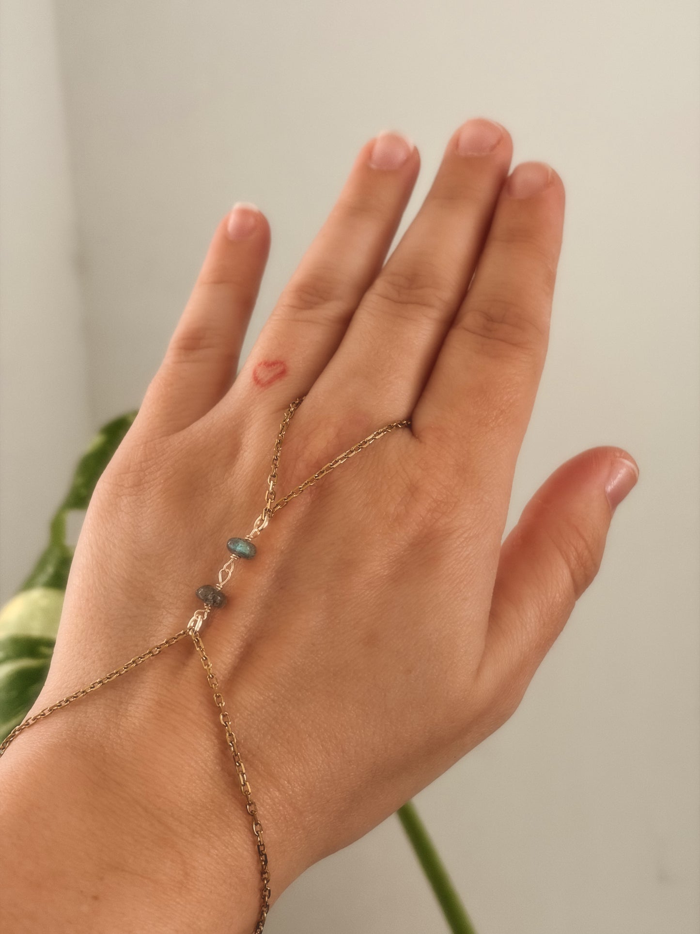 Gold stainless steel handchain bracelet with Labradorite beads on a person's wrist against a neutral background.