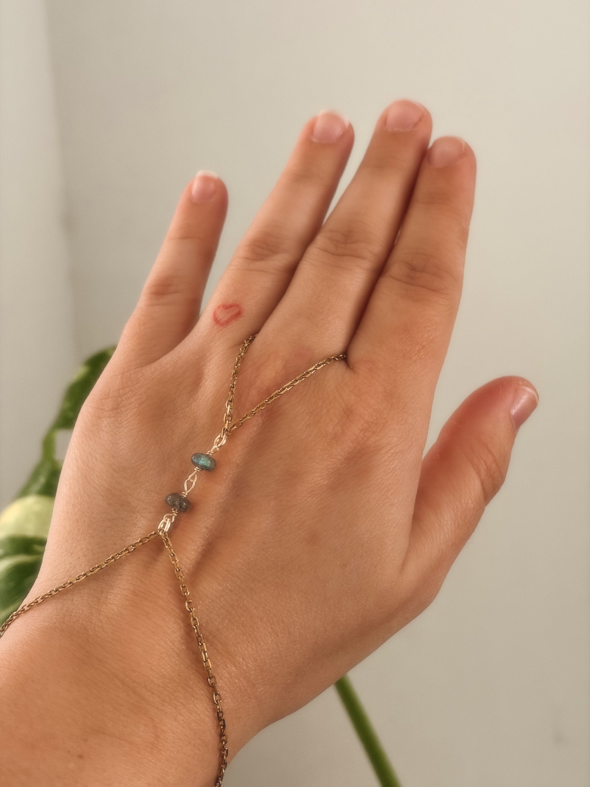 Gold stainless steel handchain bracelet with Labradorite beads on a person's wrist against a neutral background.