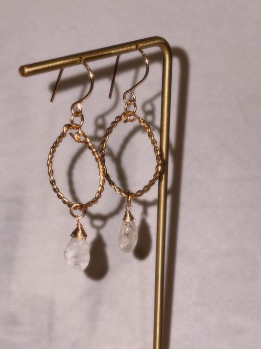 Gold hoop earrings with clear Rainbow Moonstone stones on a light background.