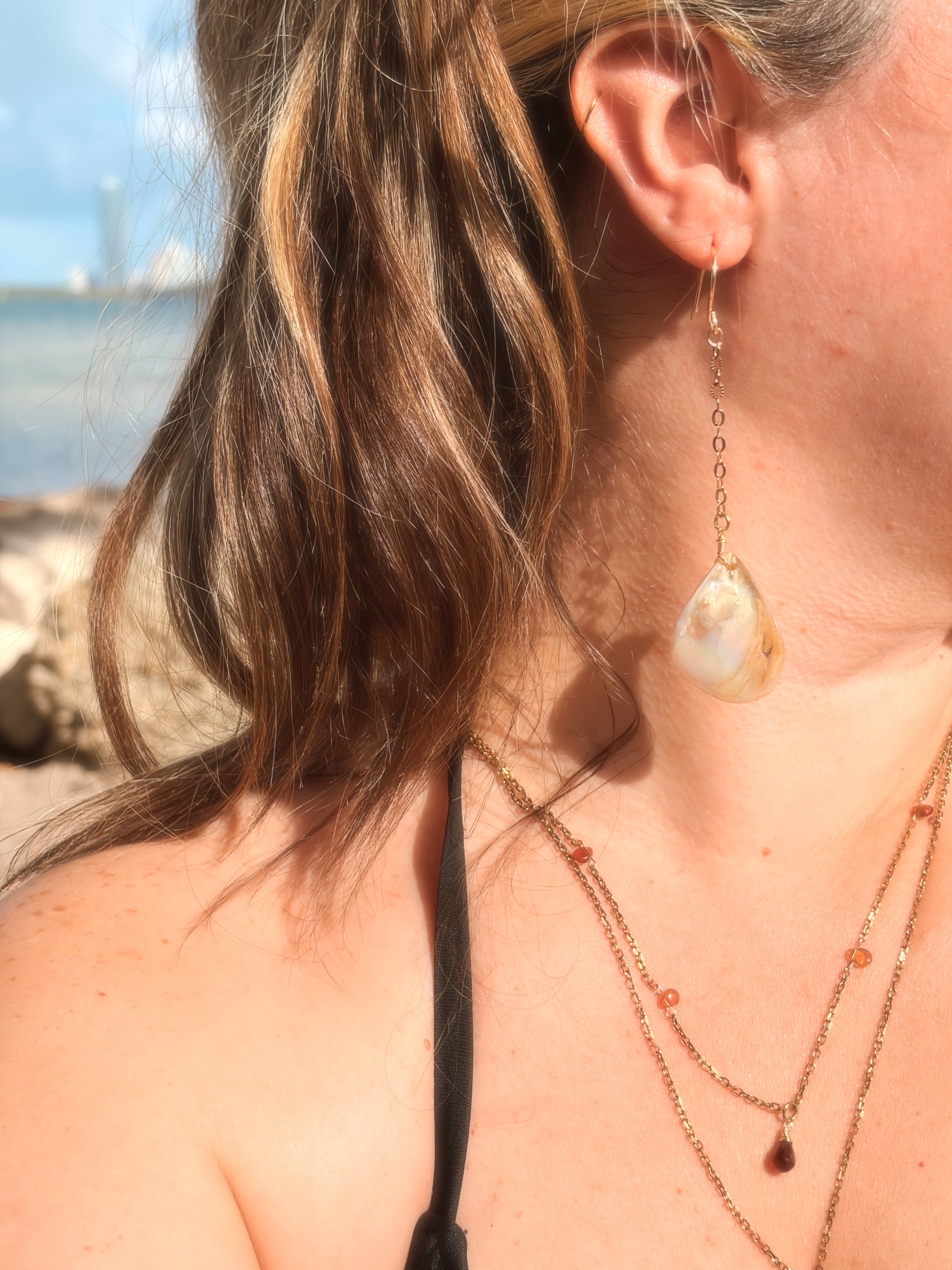 Close-up of a woman wearing layered stainless steel and crystal necklaces and  gold pearl earring.