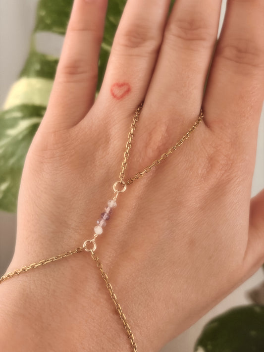 Gold Stainless Steel tarnish resistant handchain with Fluorite crystal beads on a person's hand against a blurred background with a monsterra plant.