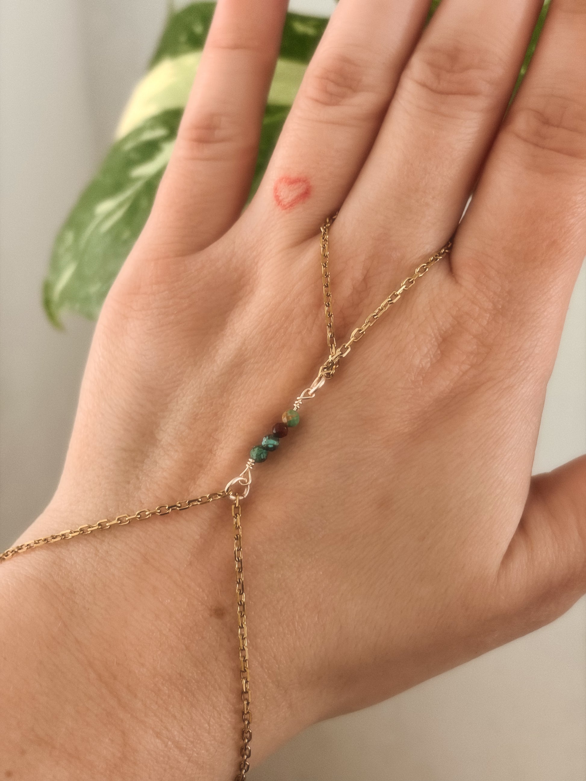 Gold hand chain bracelet with african turquoise beads on a person's hand against a neutral background