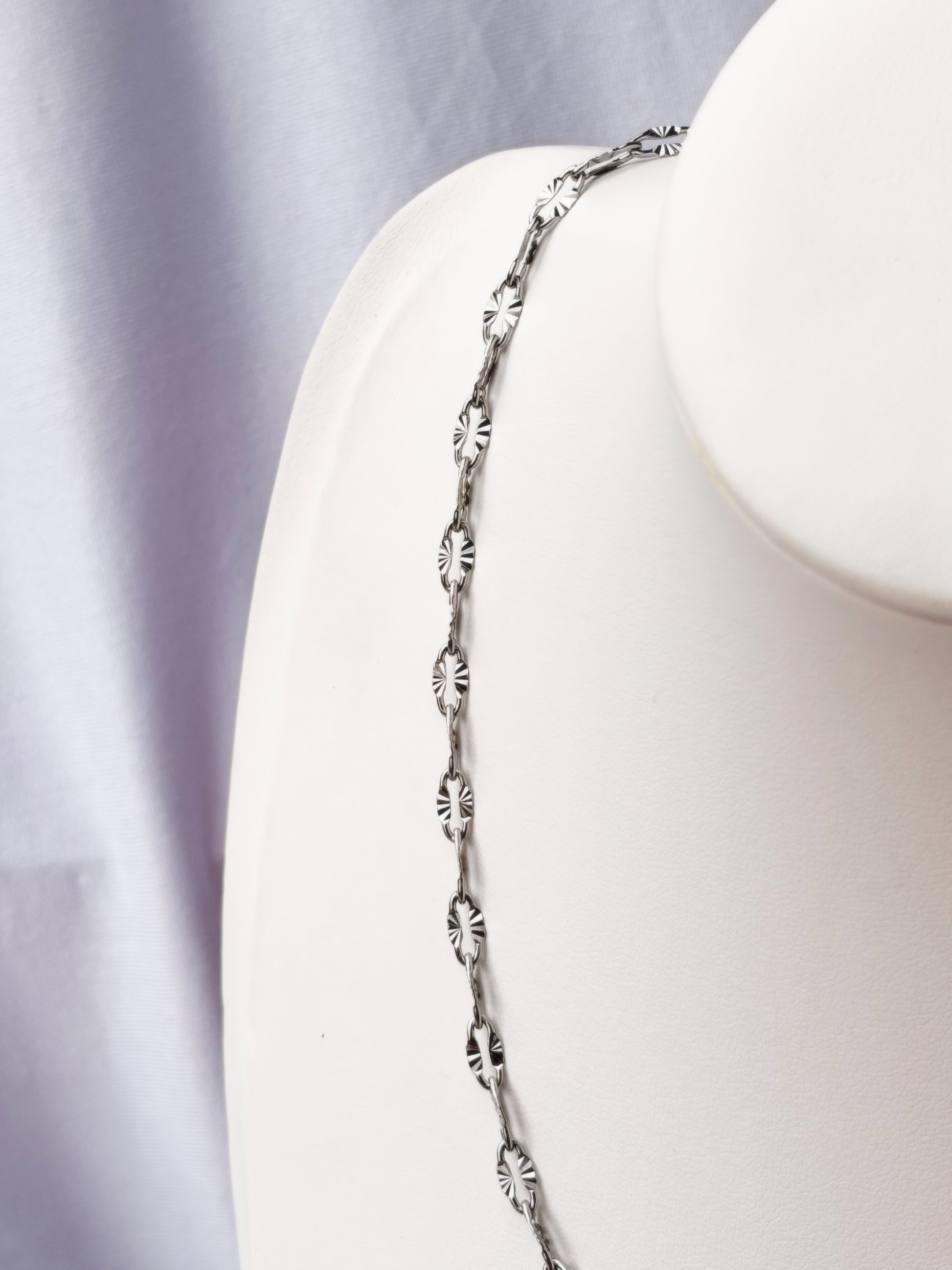 Silver necklace on a white necklace holder with a white background