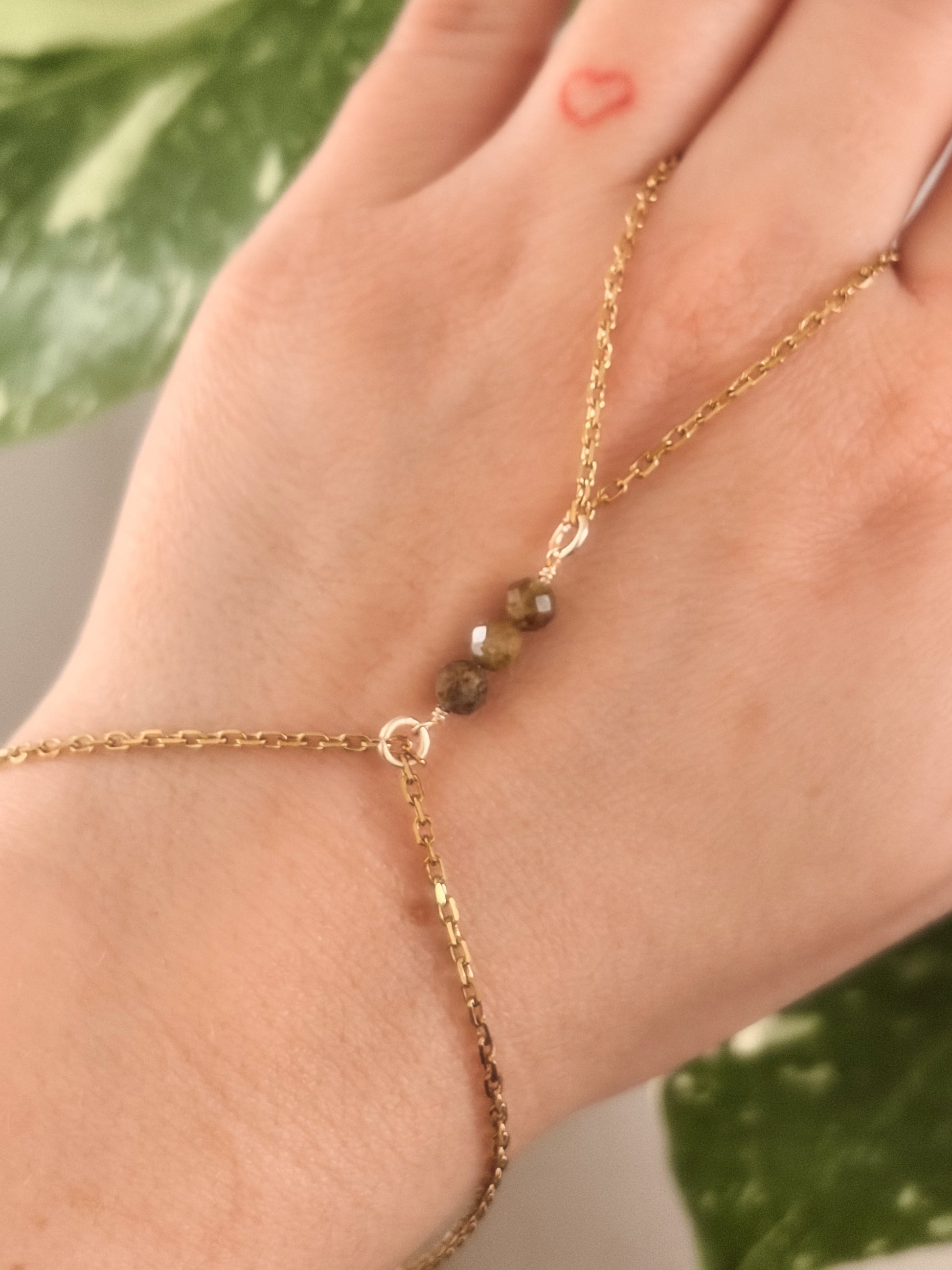 Gold Stainless Steel tarnish resistant handchain with Green Garnet crystal beads on a person's hand.