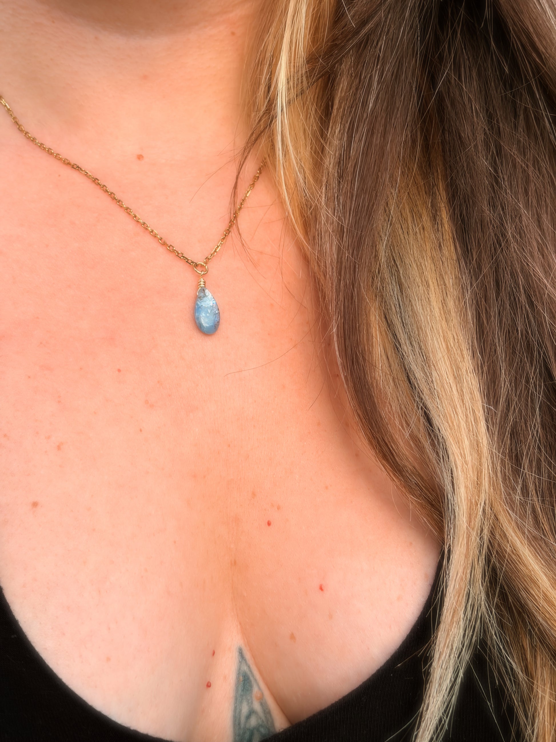 Gold Stainless Steel Necklace holding a Blue Kyanite gemstone on somone's neck with a black top.