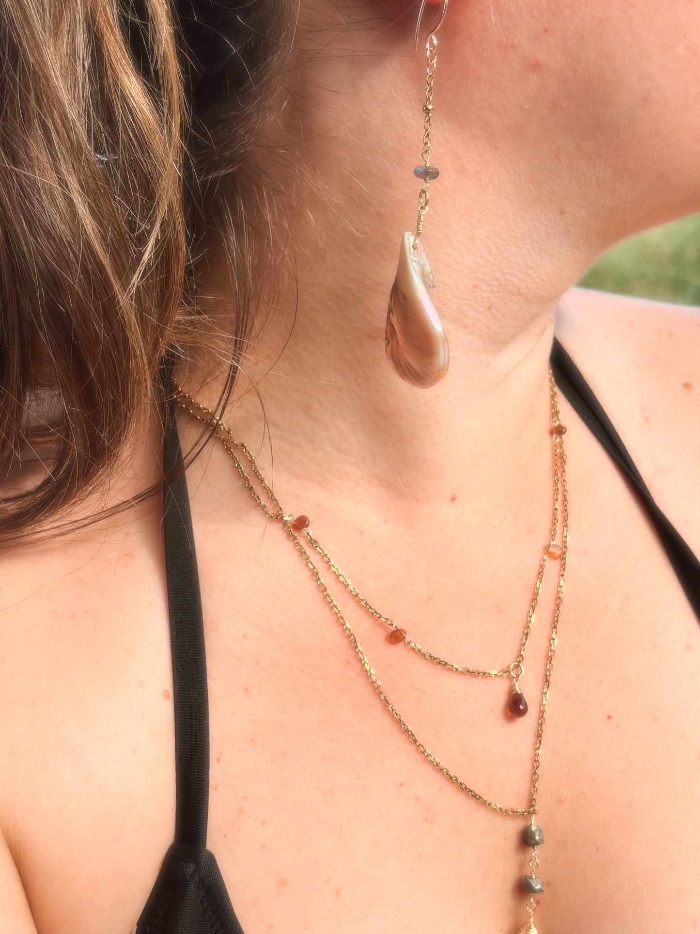 Person wearing layered crystal necklaces and Stainless Steel Gold dangly shell earrings with labradorite bead crystal.