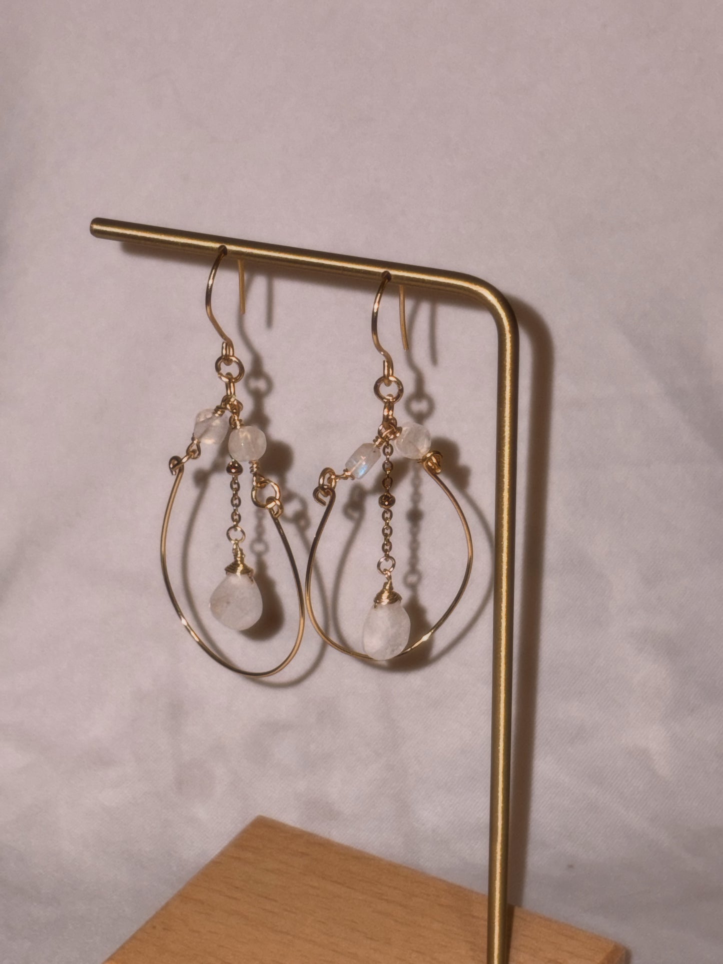Gold brass and stainless steel hoop earrings with small Rainbow Moonstone beads on a gold stand against a light background. 