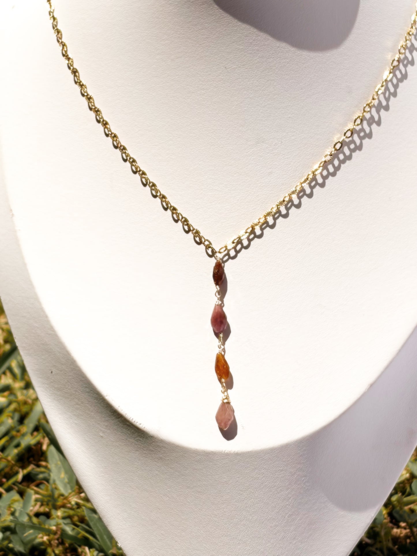 A gold chain necklace, lariat style necklace with pink and orange tourmaline stone beads, displayed on a white jewelry bust.