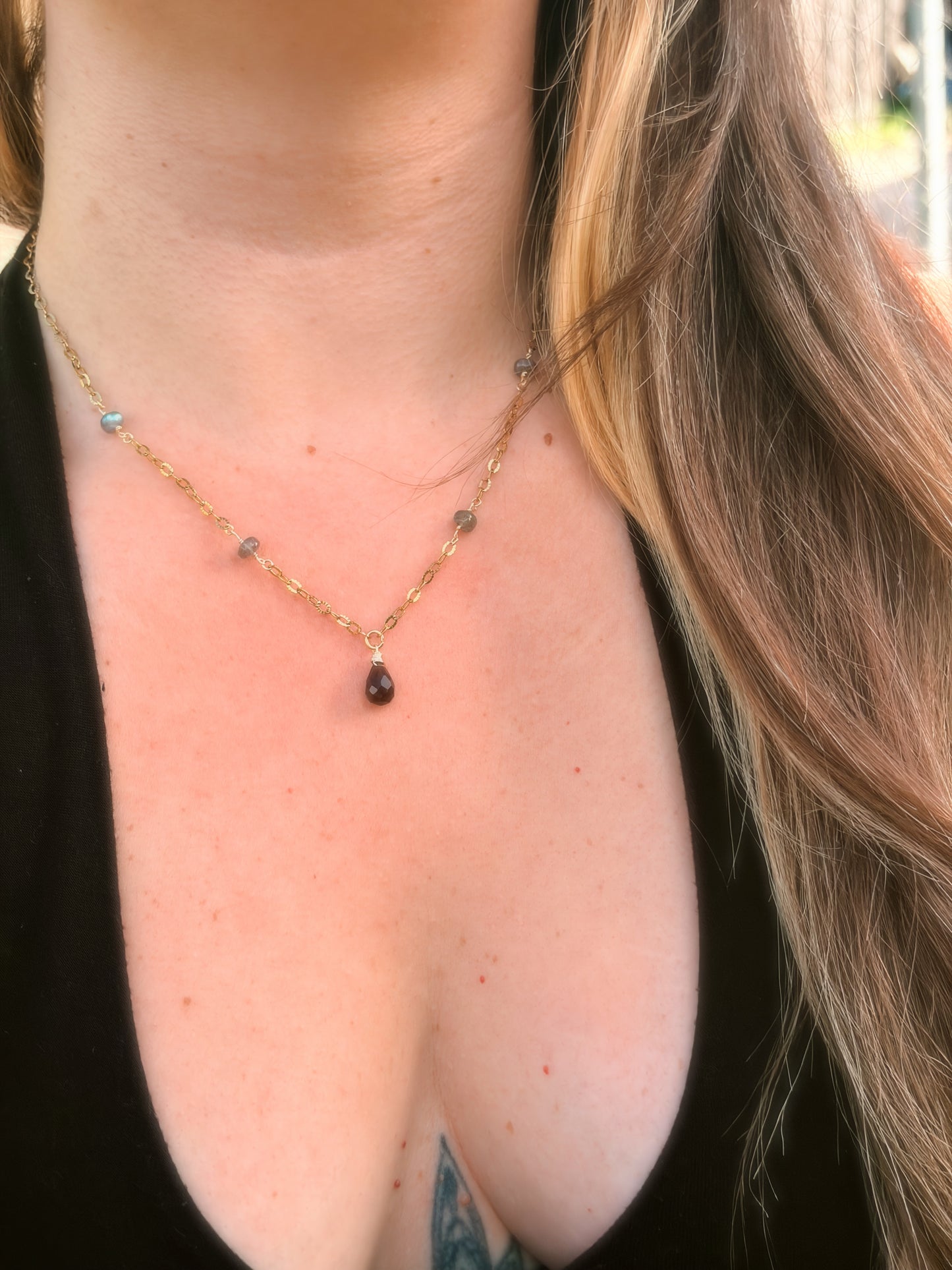 Close-up of a smoky quartz and labradorite stainless steel gold necklace with a teardrop pendant on a person wearing a black top.