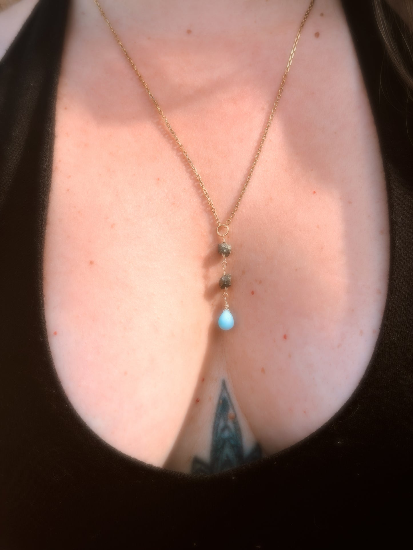 Close-up of a person wearing a delicate gold stainless steel necklace with Pyrite and Larimar beads on a plain background wearing a black top.