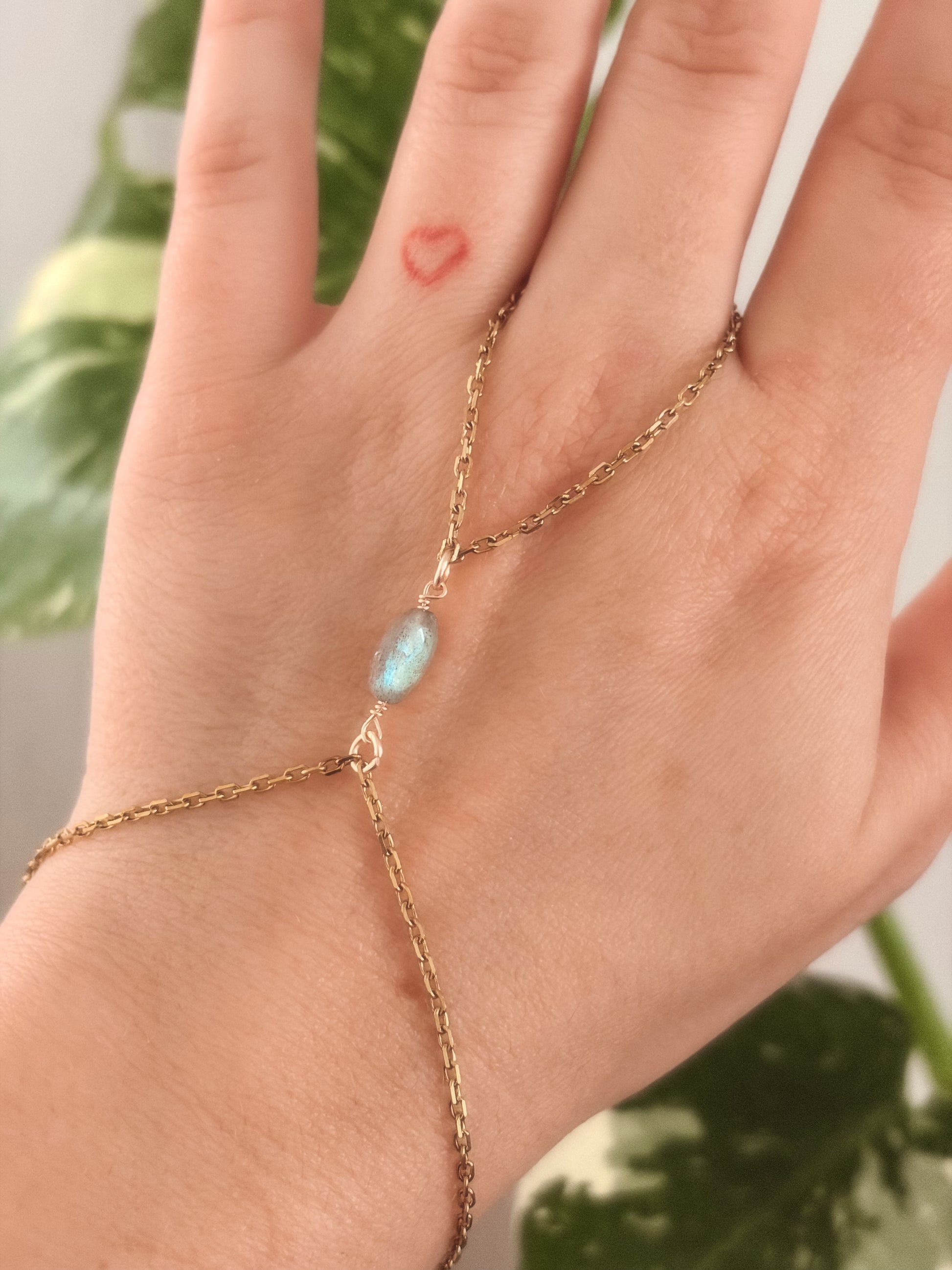 Gold stainless steel handchain bracelet with Labradorite beads on a person's wrist against a neutral background.