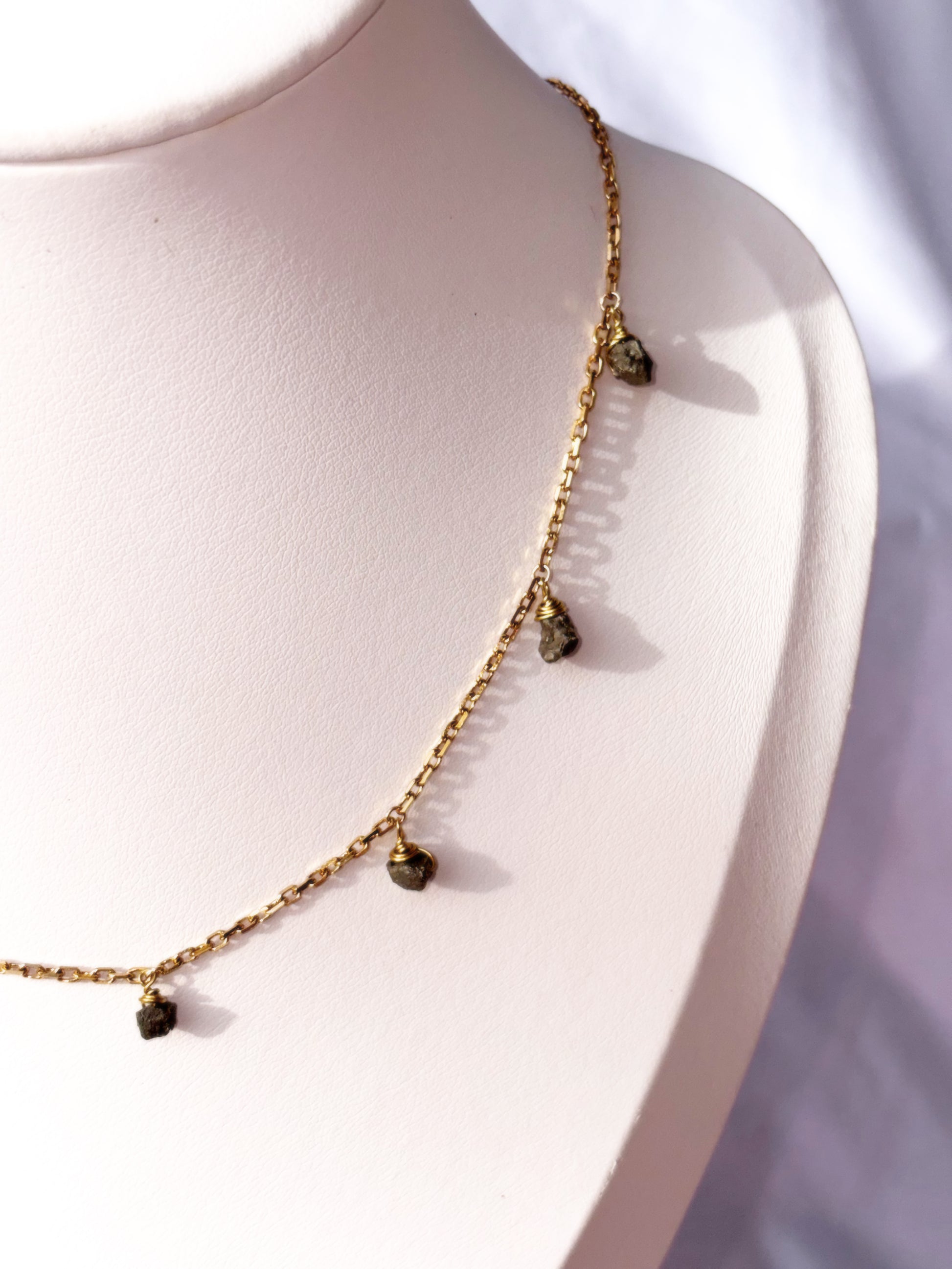 Close up of Stainless Steel Gold necklace with small Pyrite raw beads stones on a white stand.