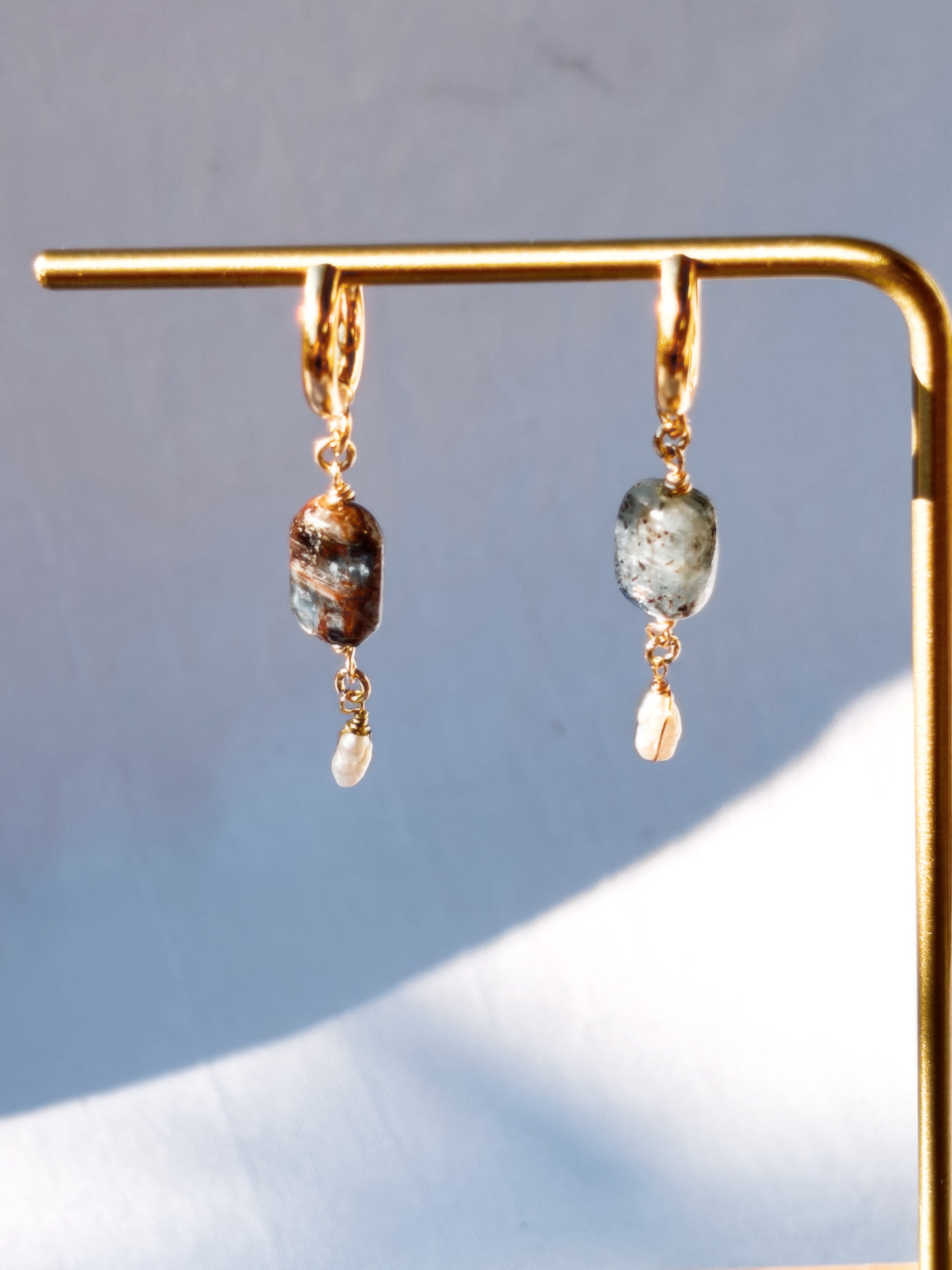 Gold earrings with Blue Kyanite and Faux Pearl gemstones on a stand against a light background