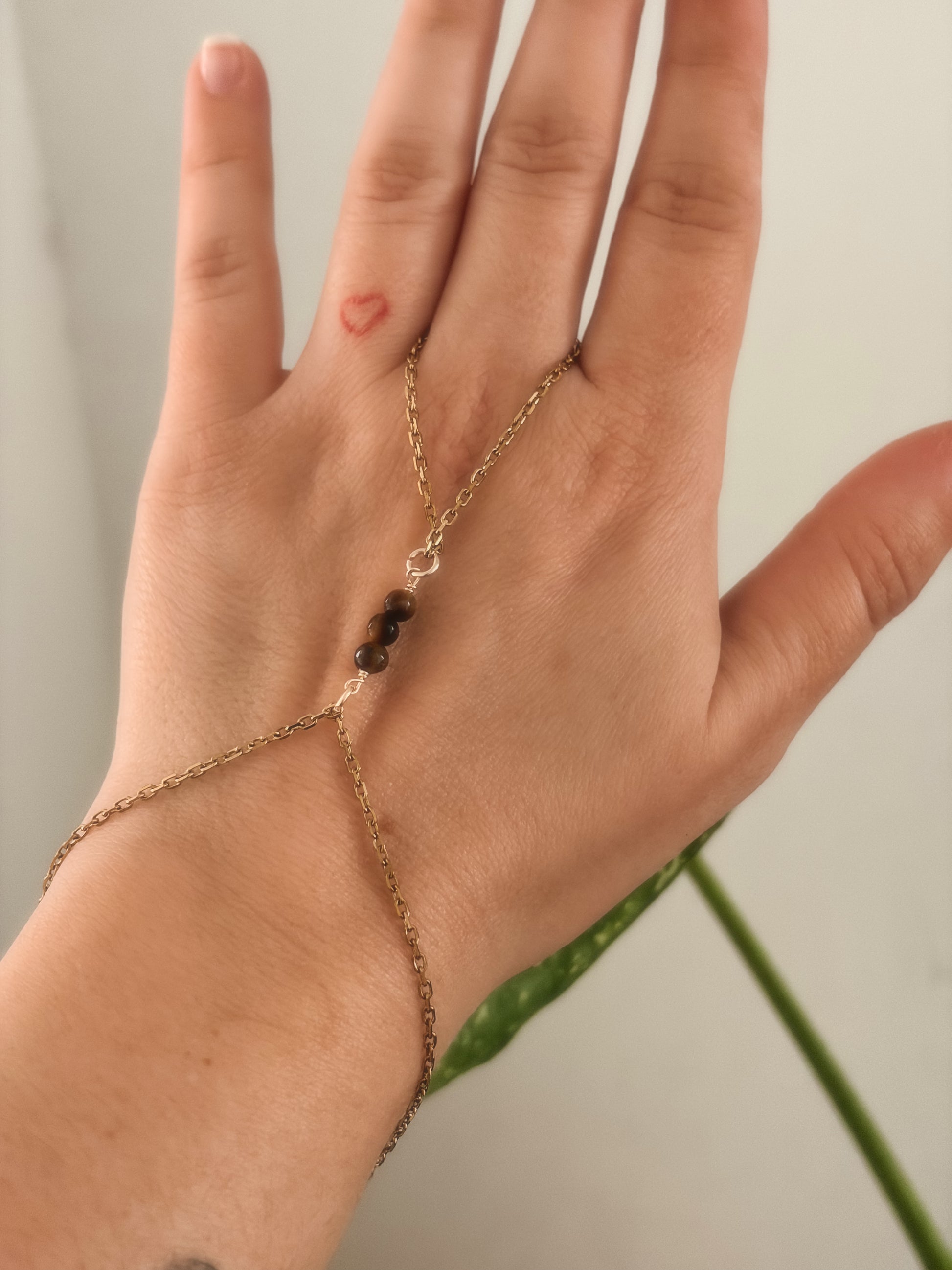 Gold stainless steel handchain bracelet with Tiger Eye beads on a person's wrist against a neutral background.