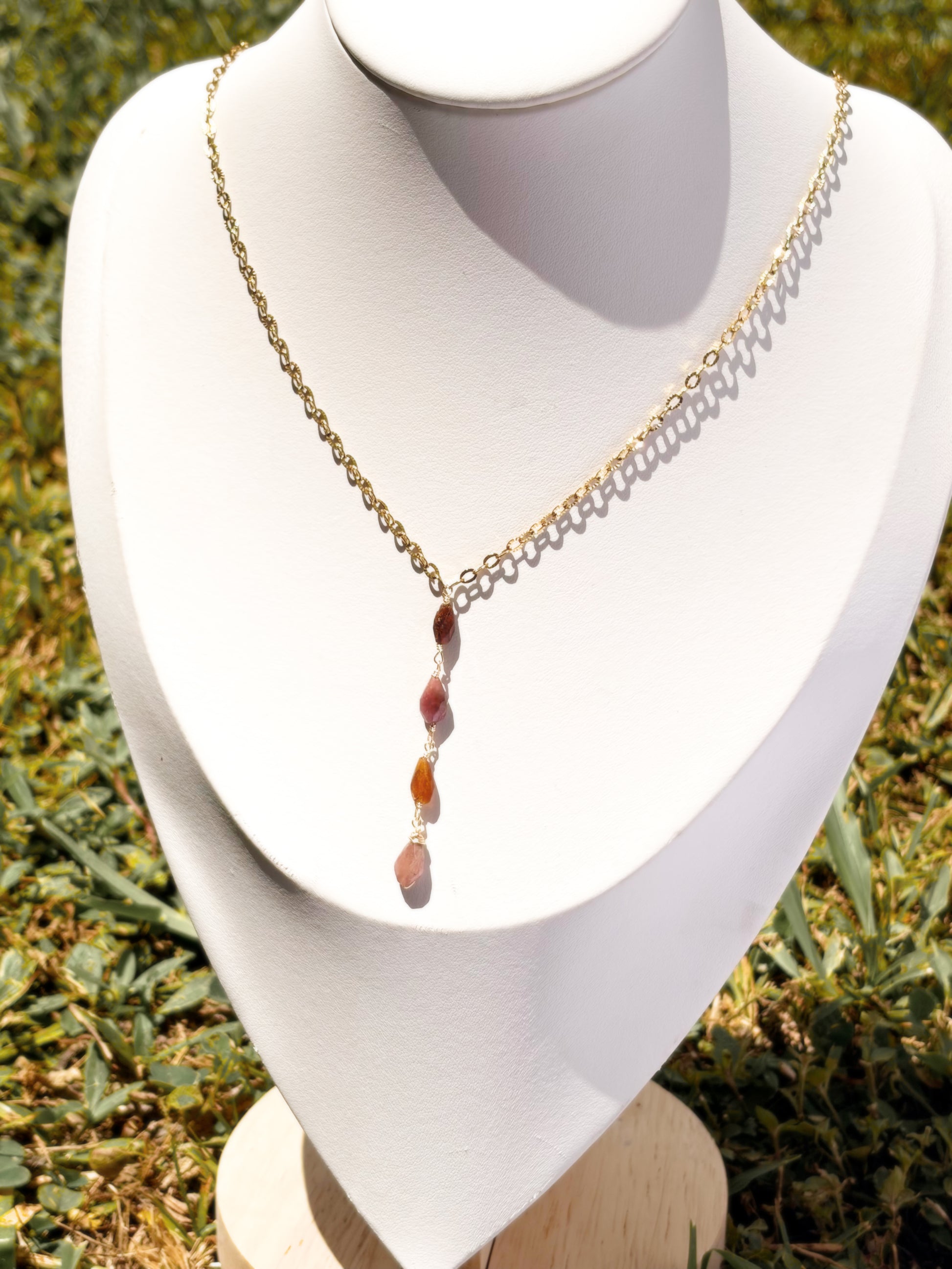 A gold chain necklace, lariat style necklace with pink and orange tourmaline stone beads, displayed on a white jewelry bust.