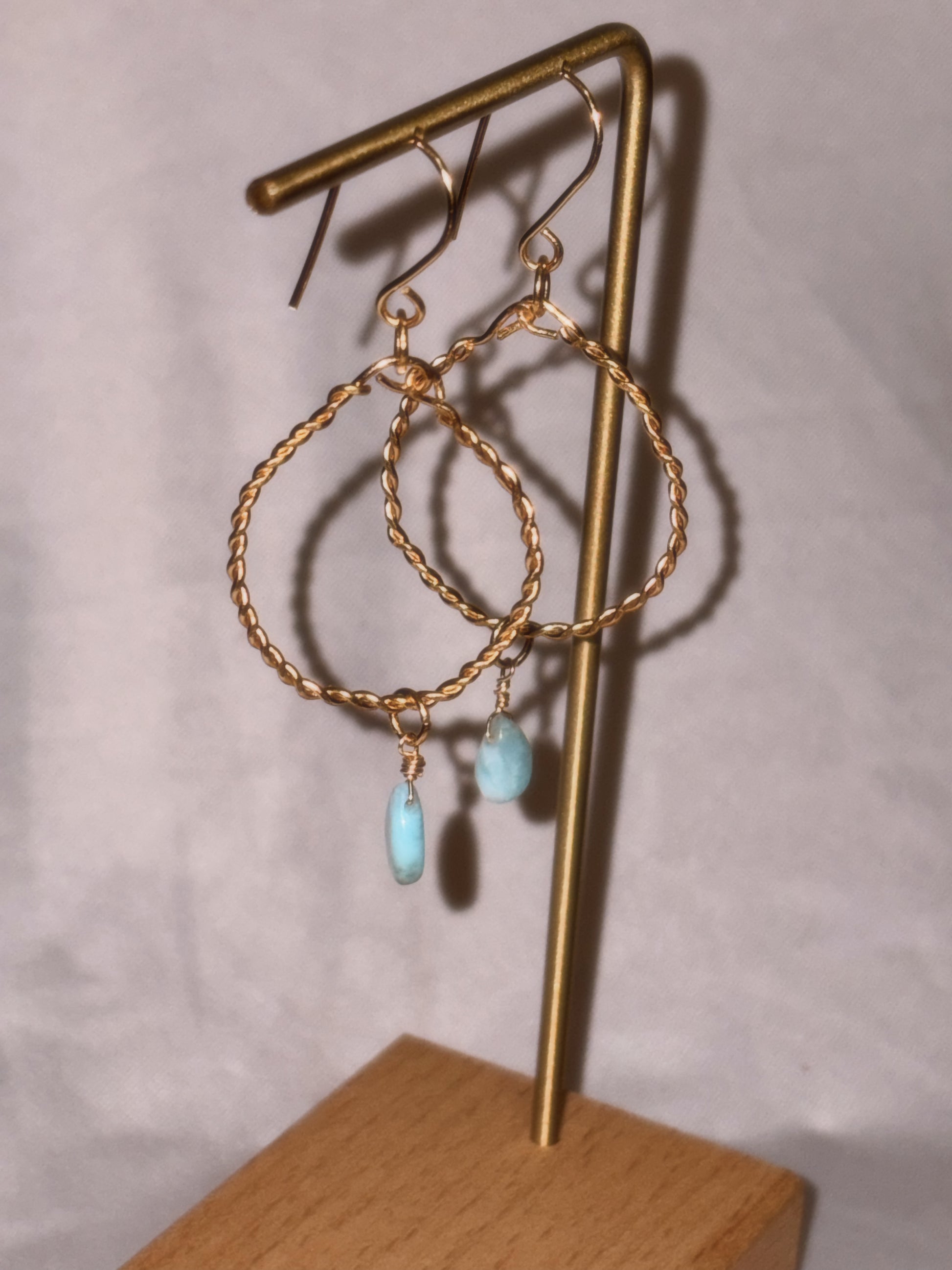Gold brass and stainless steel hoop earrings with turquoise Larimar stones on a light background.