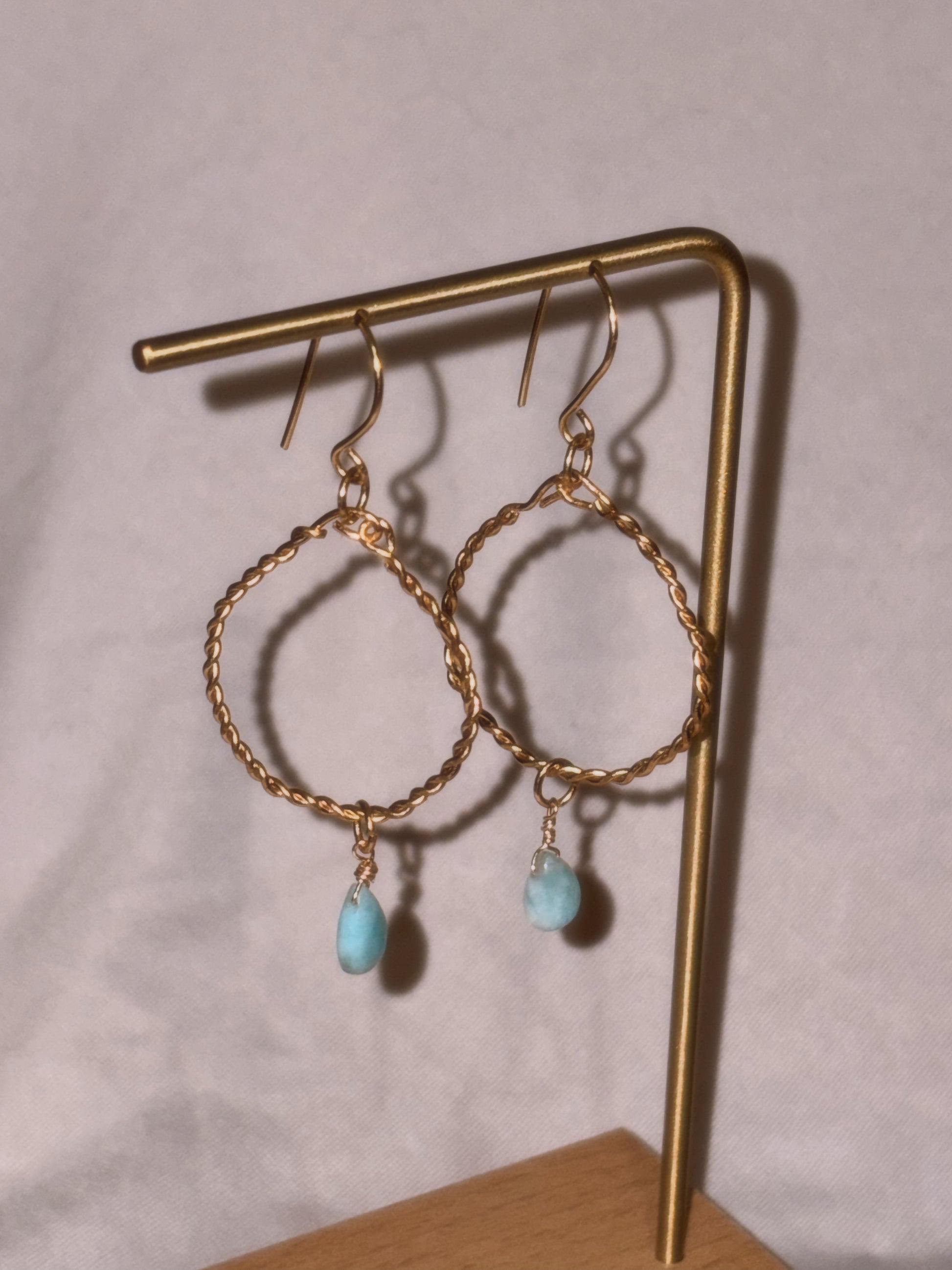 Gold brass and stainless steel hoop earrings with turquoise Larimar stones on a light background.