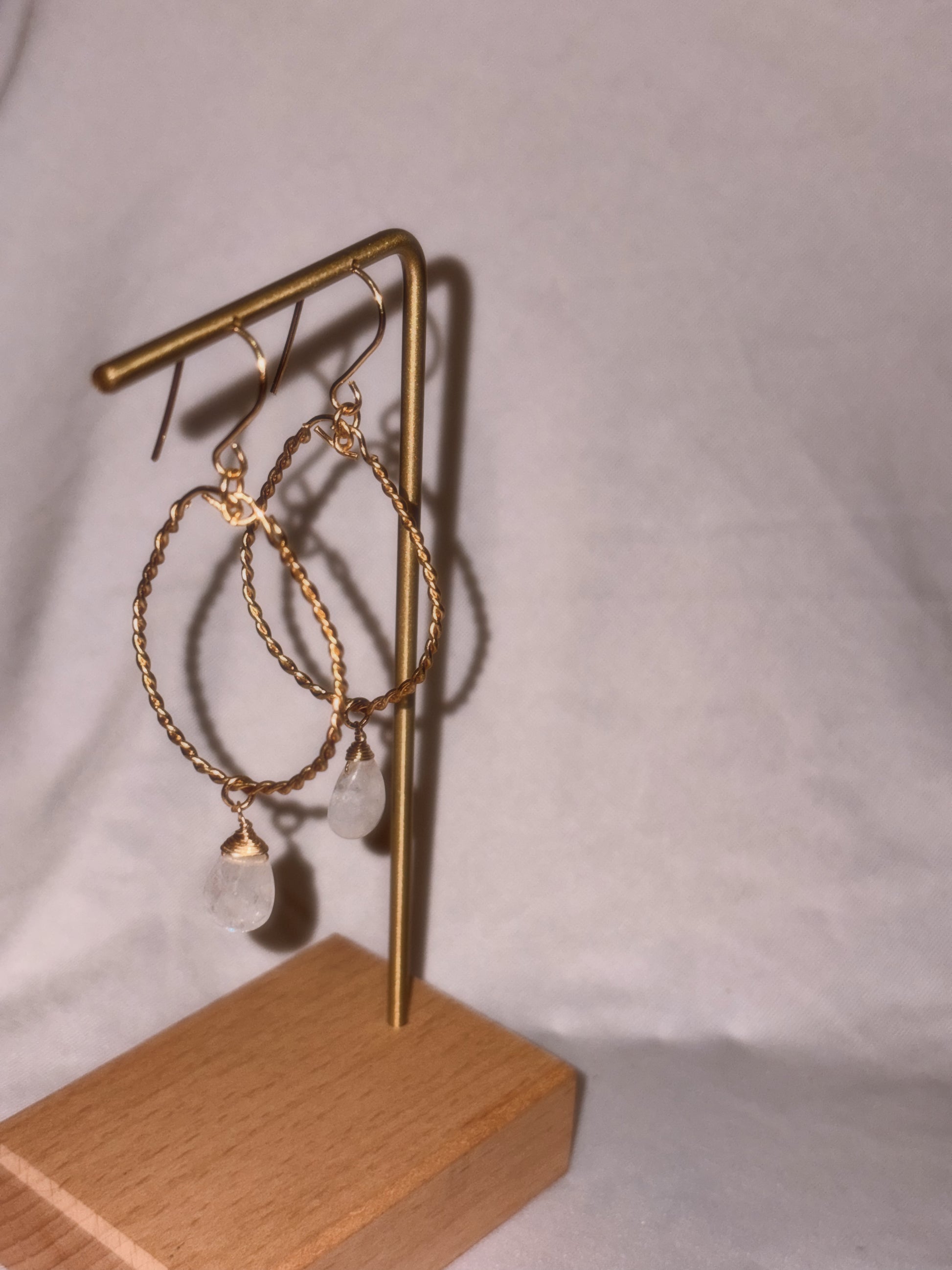 Gold hoop earrings with clear Rainbow Moonstone stones on a light background.