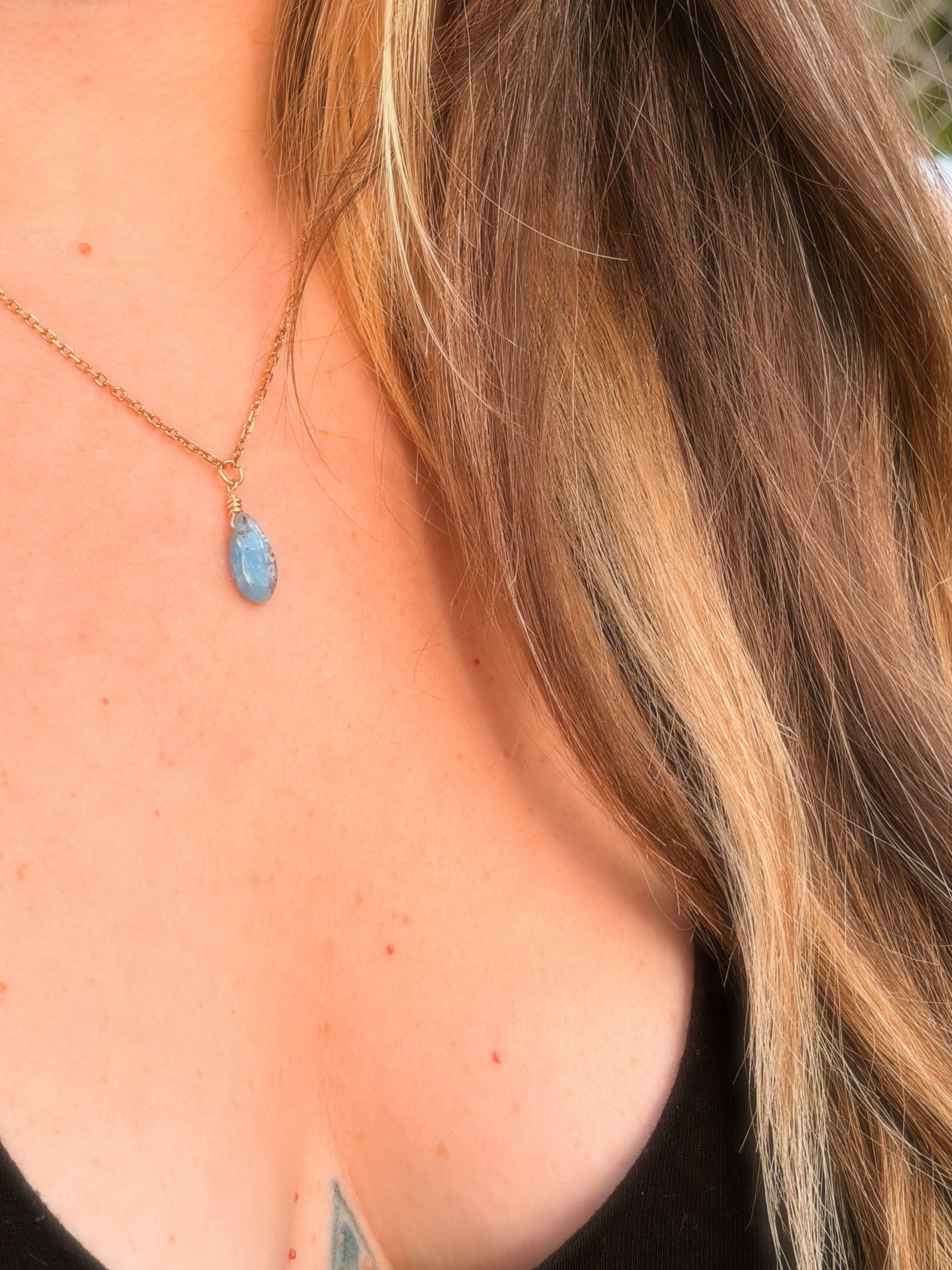 Gold Stainless Steel Necklace holding a Blue Kyanite gemstone on somone's neck with a black top.