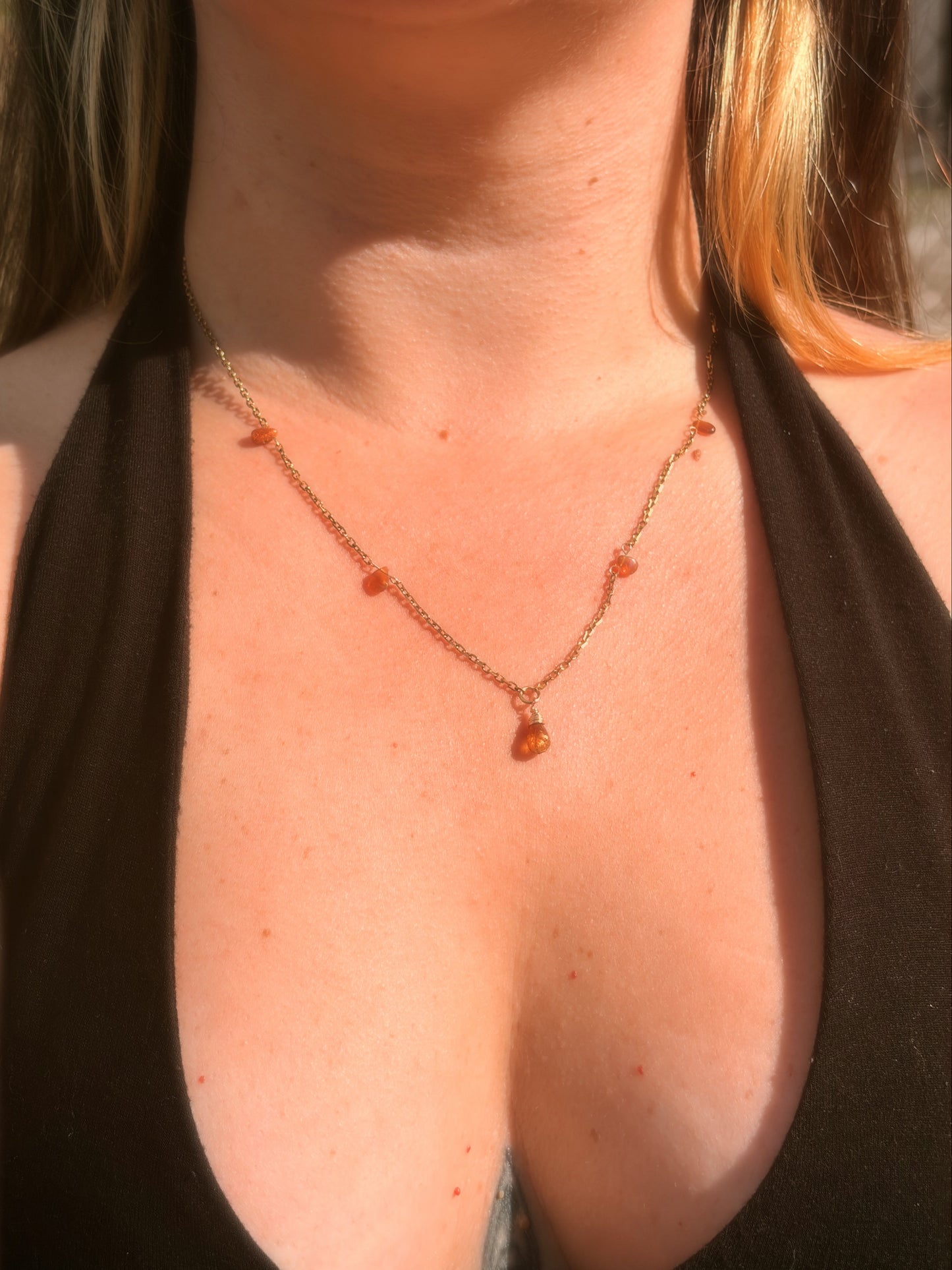 Close-up of a stainless steel gold necklace with amber-colored Tundra Tourmaline and Ethiopian Opal beads on a person wearing a black top.