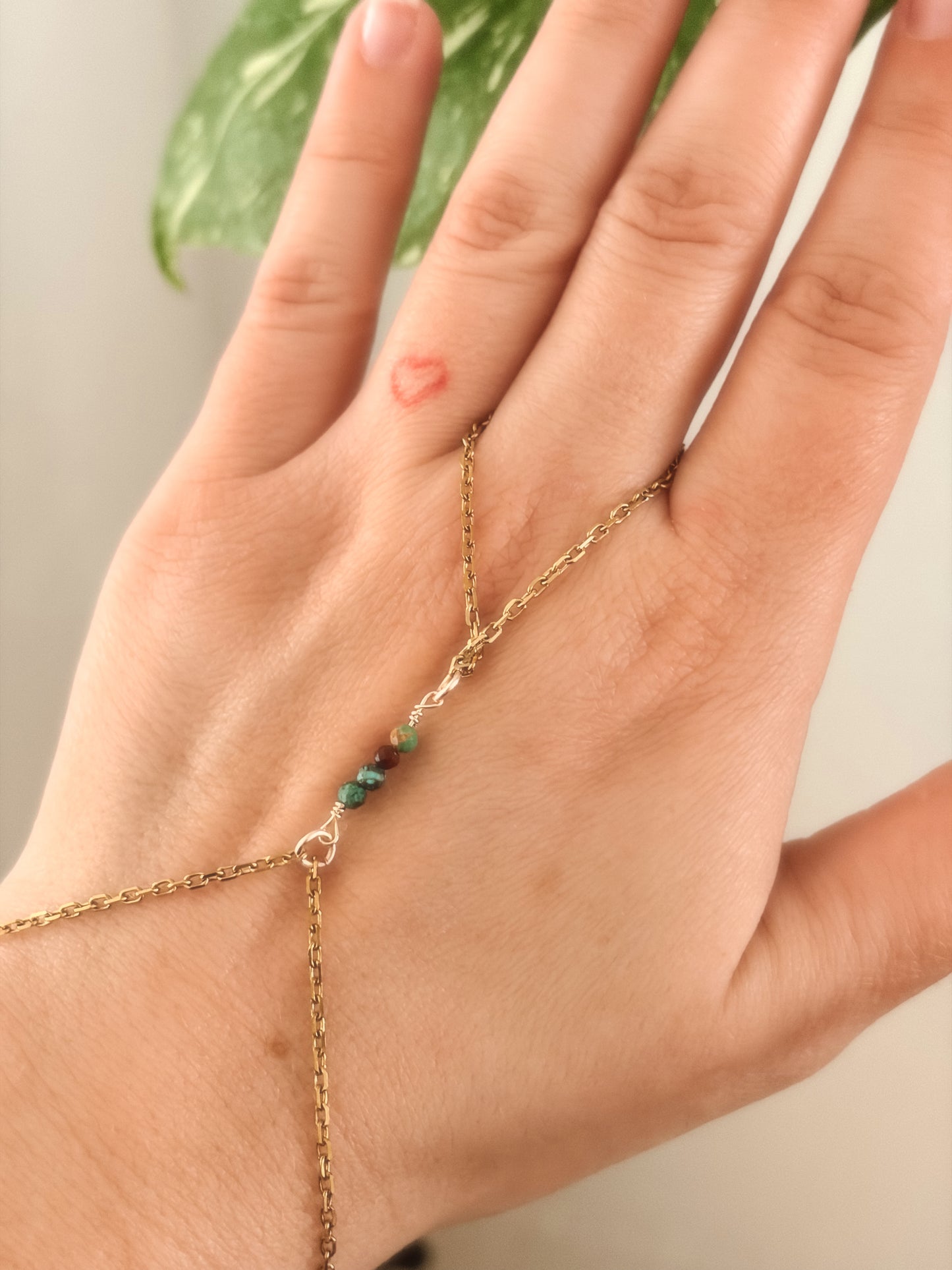 Hand wearing a delicate gold necklace with african turquoise beads against a neutral background