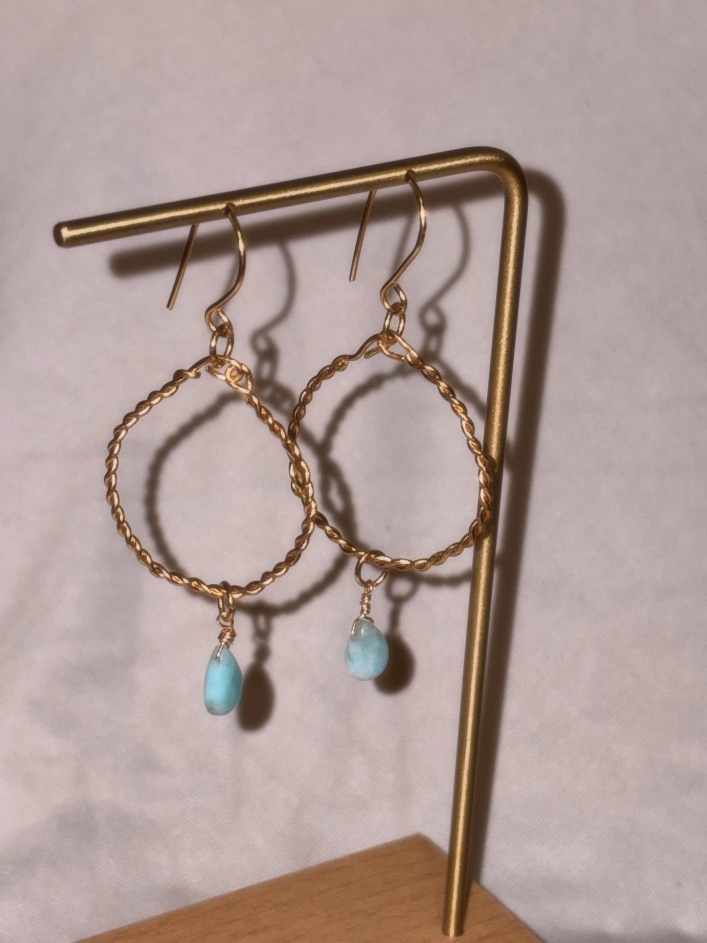Gold brass and stainless steel hoop earrings with turquoise Larimar stones on a light background.
