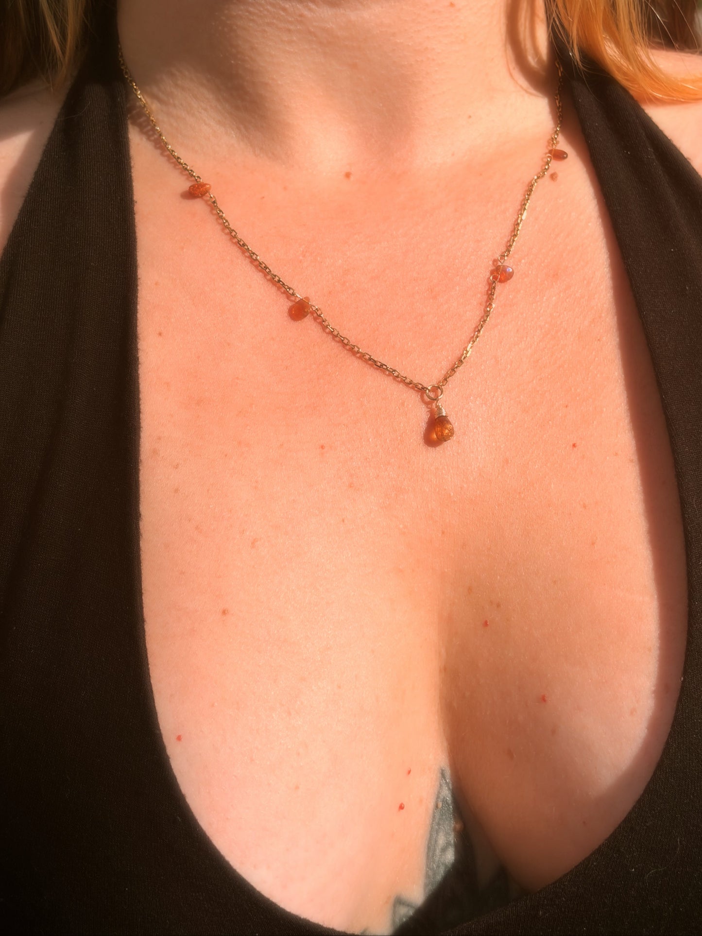 Close-up of a stainless steel gold necklace with amber-colored Tundra Tourmaline and Ethiopian Opal beads on a person wearing a black top.