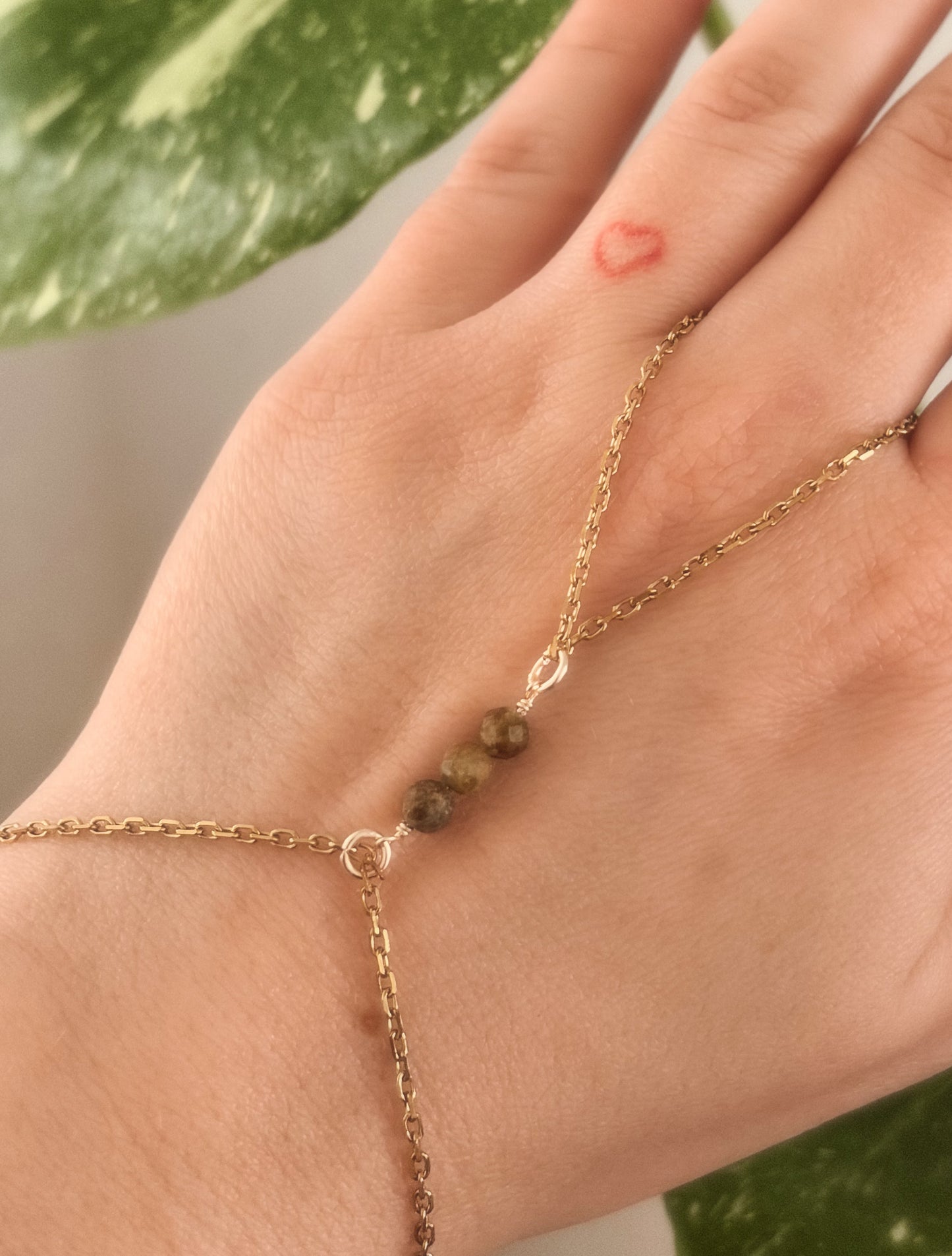 Gold Stainless Steel tarnish resistant handchain with Green Garnet crystal beads on a person's hand.