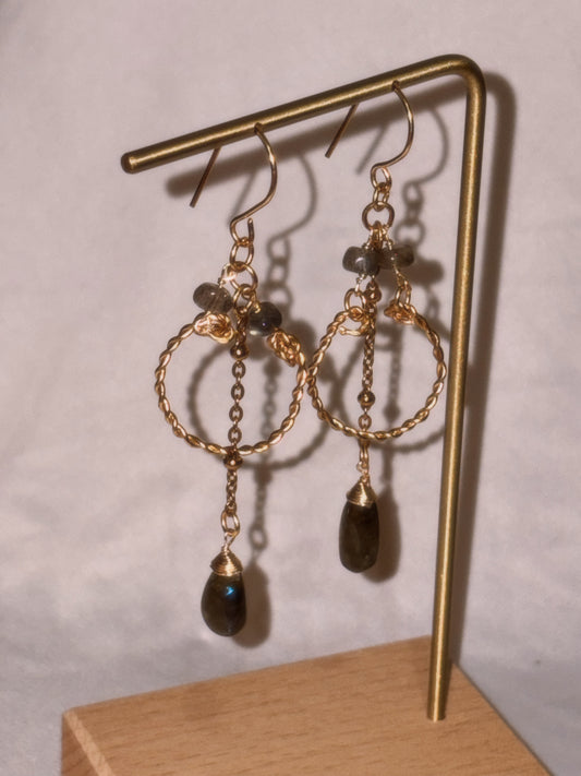 Gold brass and stainless steel hoop earrings with small and teardrop shaped Labradorite beads on a gold stand against a light background. 