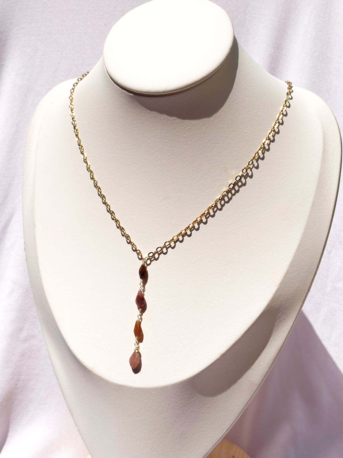 A gold chain necklace, Y lariat style necklace with pink and orange tourmaline stone beads, displayed on a white jewelry bust.