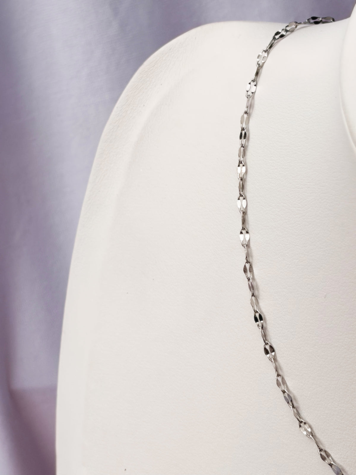 Silver chain necklace on a white mannequin bust against a white  background