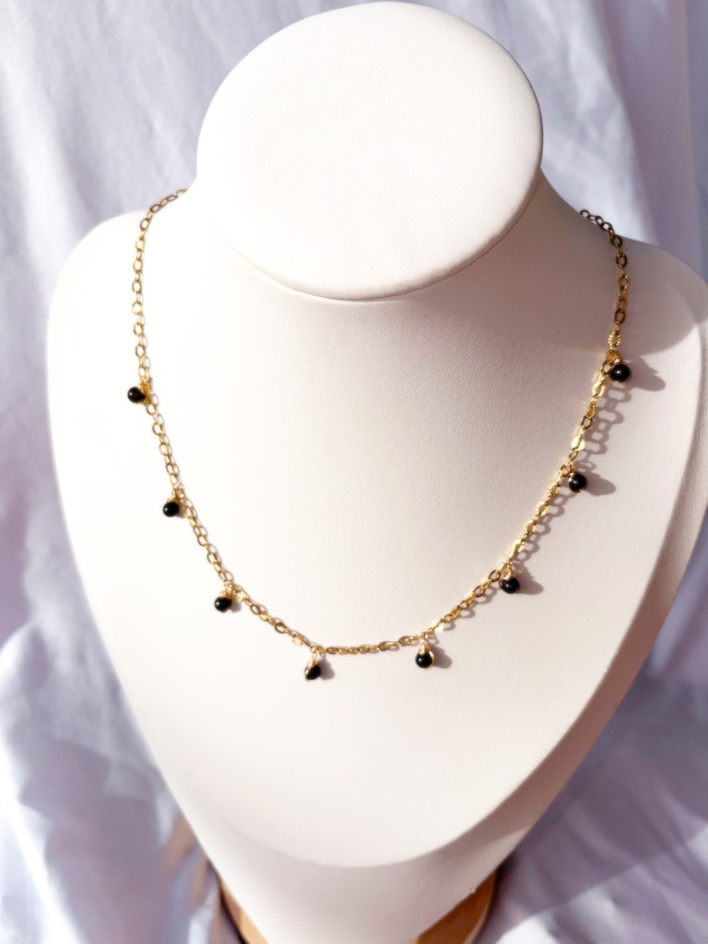 Gold Stainless Steel necklace with black gold sheen obsidian beads on a white stand against a light background.