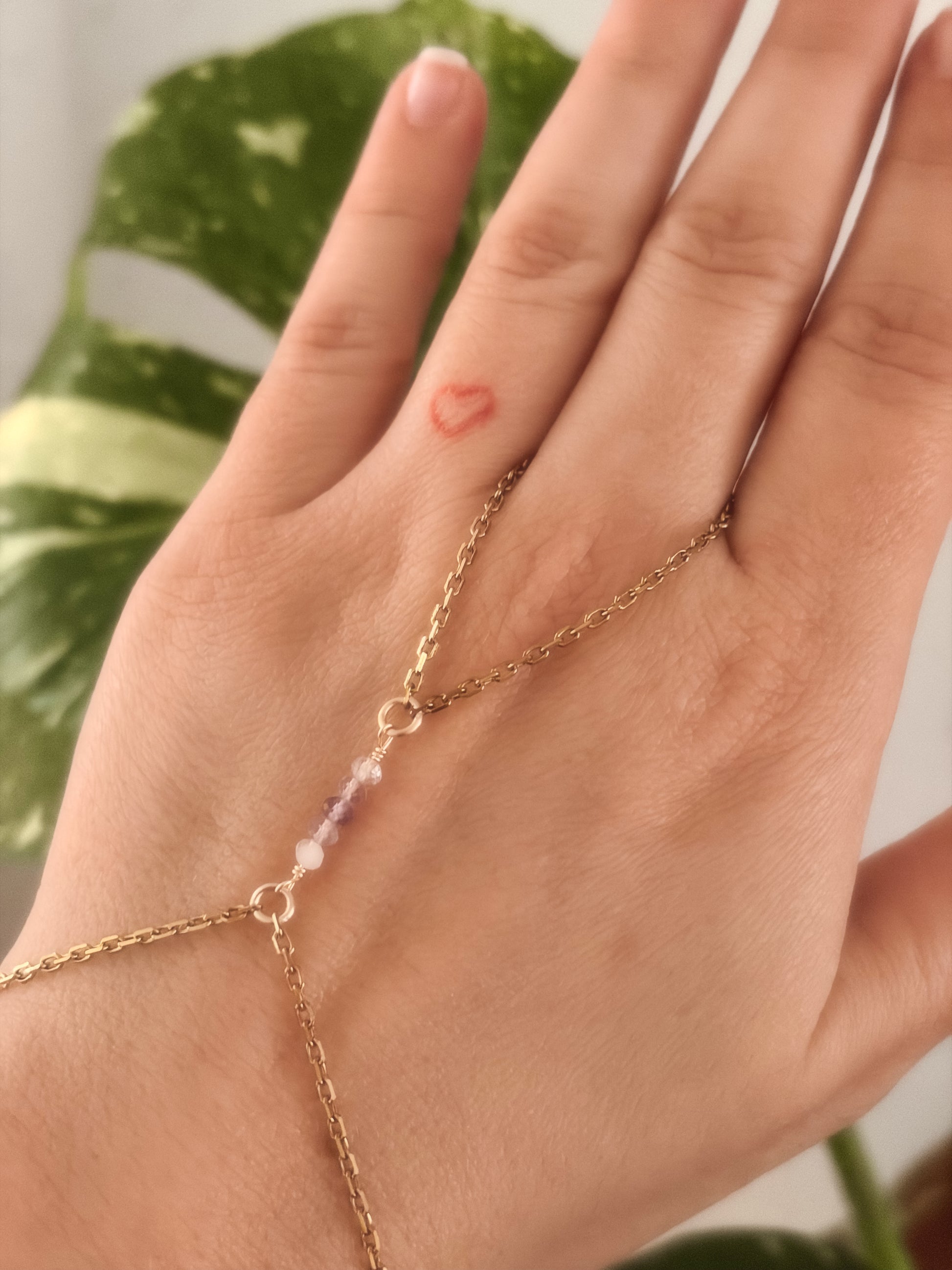 Gold Stainless Steel tarnish resistant handchain with Fluorite crystal beads on a person's hand against a blurred background with a monsterra plant.