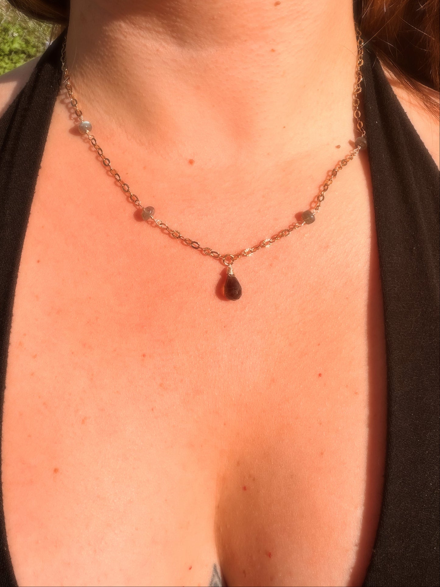 Close-up of a smoky quartz and labradorite stainless steel gold necklace with a teardrop pendant on a person wearing a black top.